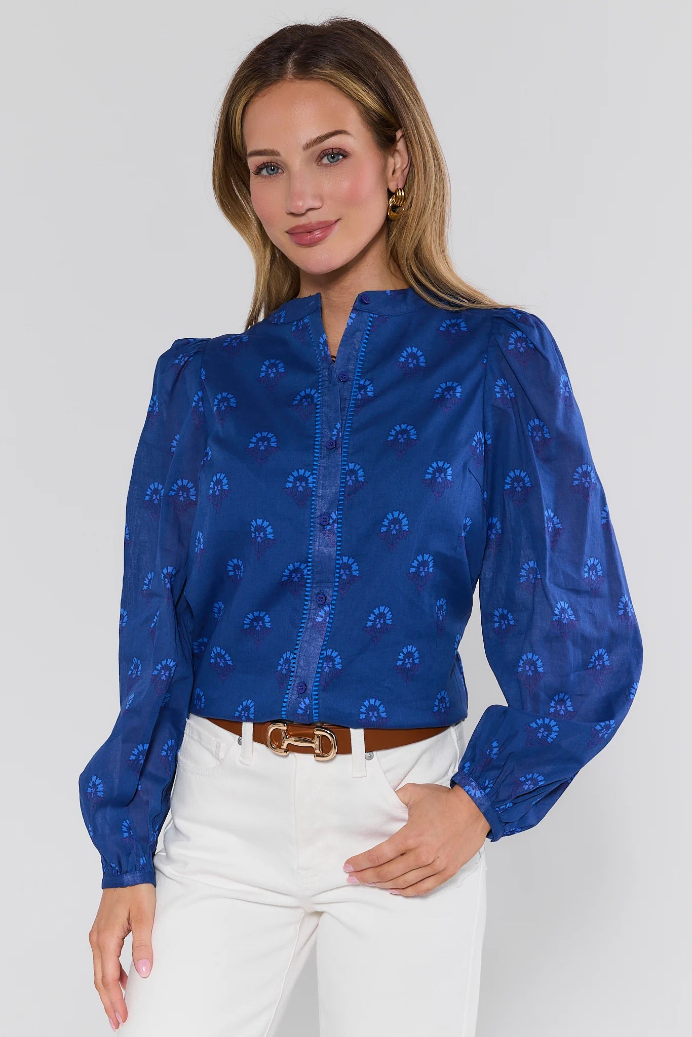 Woman wearing a blue patterned blouse and white pants on a white background