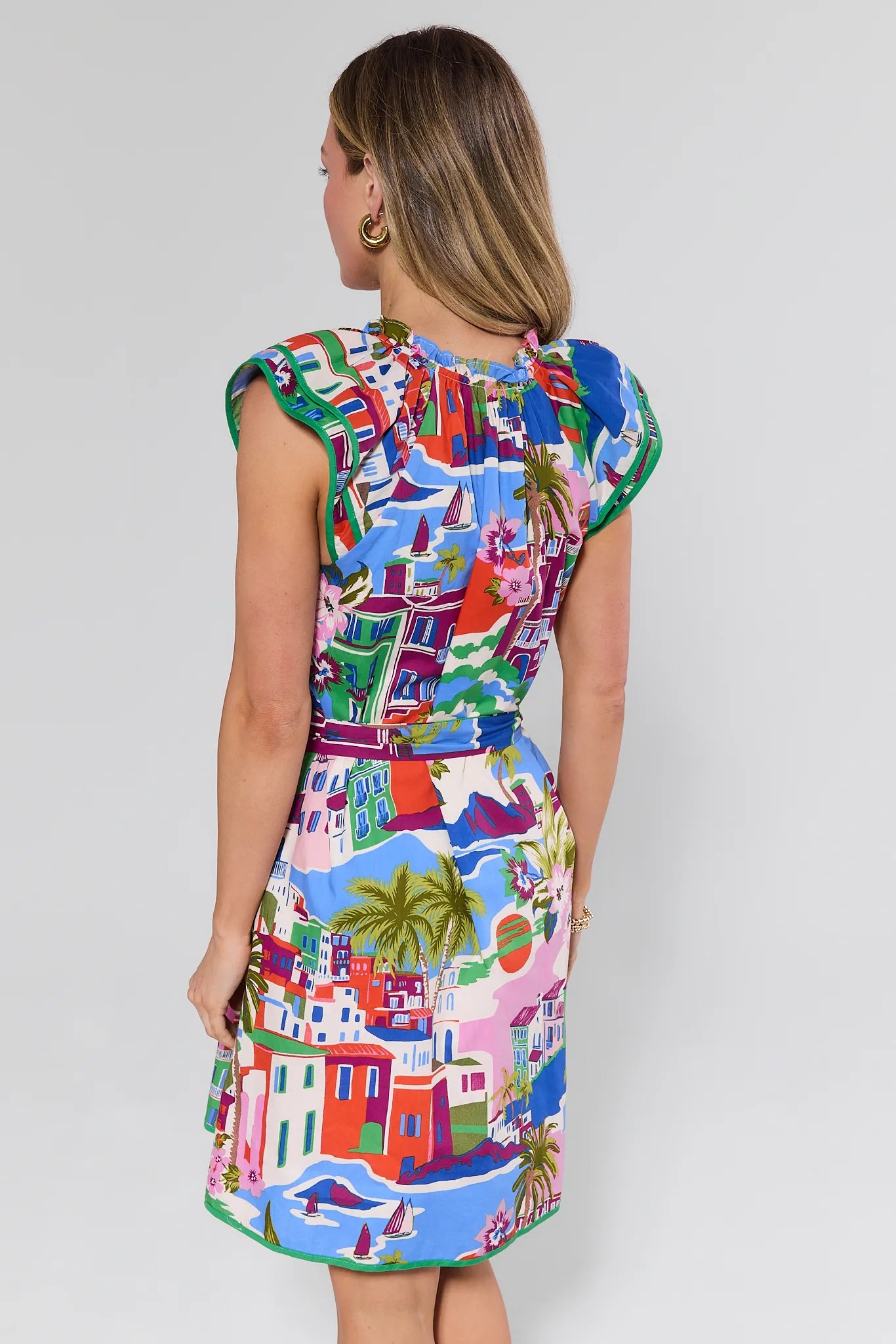 Woman wearing a colorful dress with a pattern of buildings and palm trees on a plain background