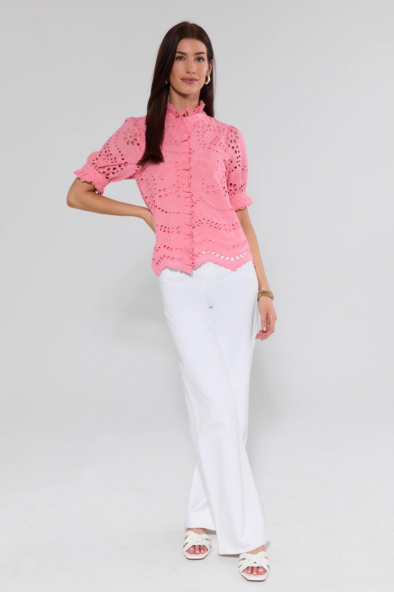 Woman wearing a pink blouse with ruffled details and white pants on a light gray background