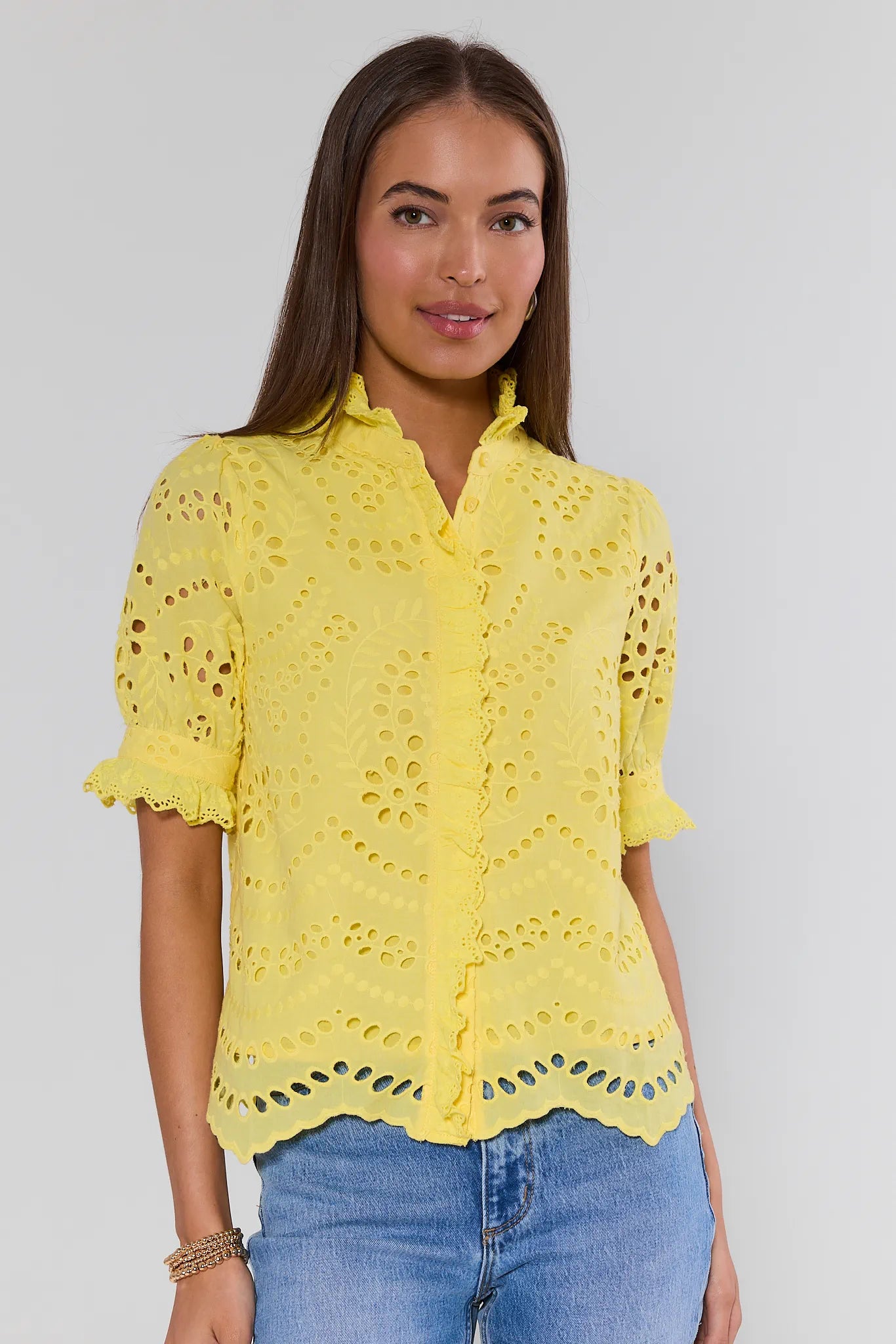 Woman wearing a yellow lace blouse and blue jeans on a plain background