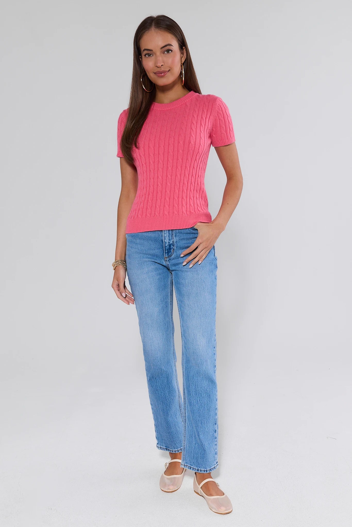Woman wearing a pink ribbed sweater and blue jeans on a white background