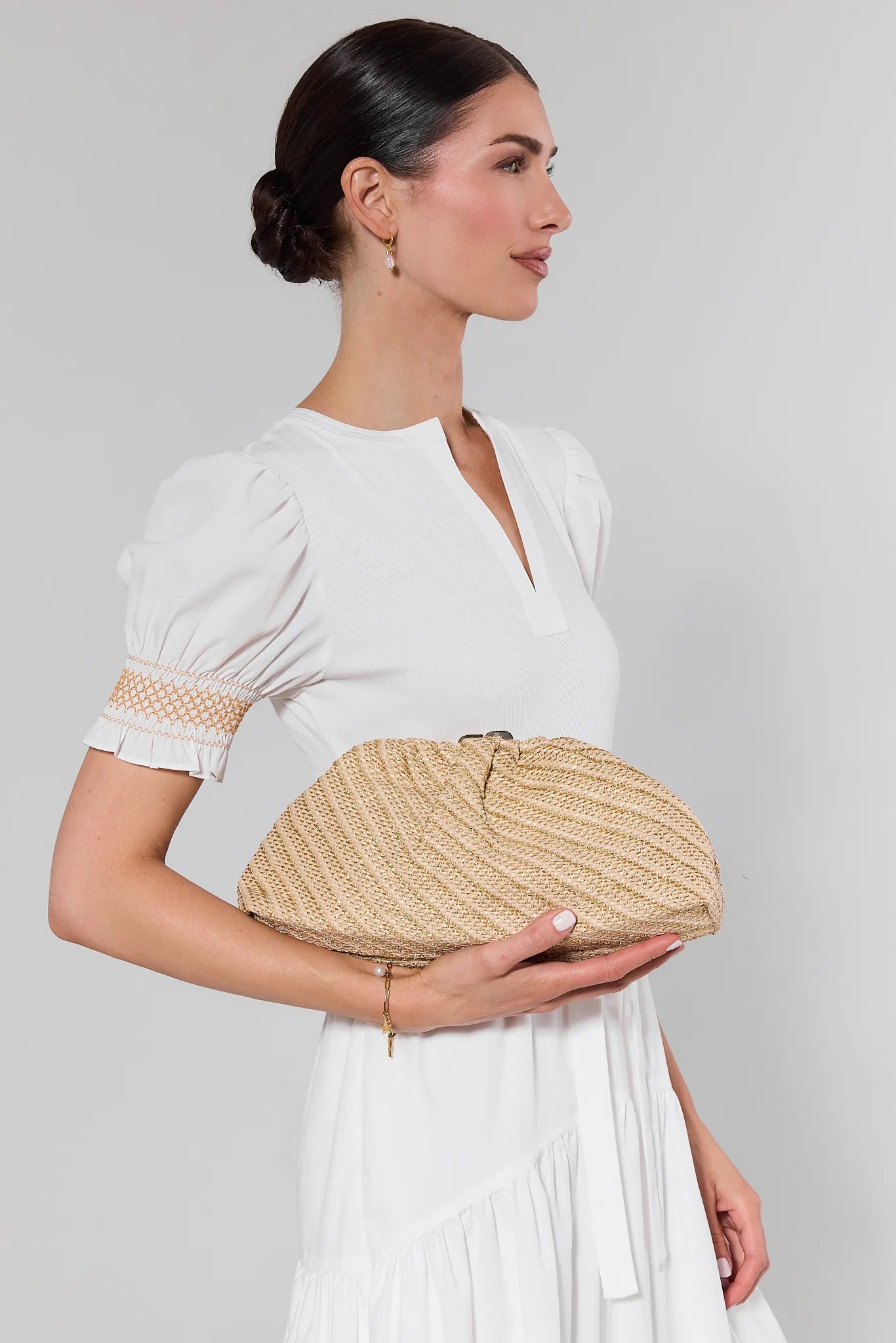 Woman holding a woven clutch bag against a plain background