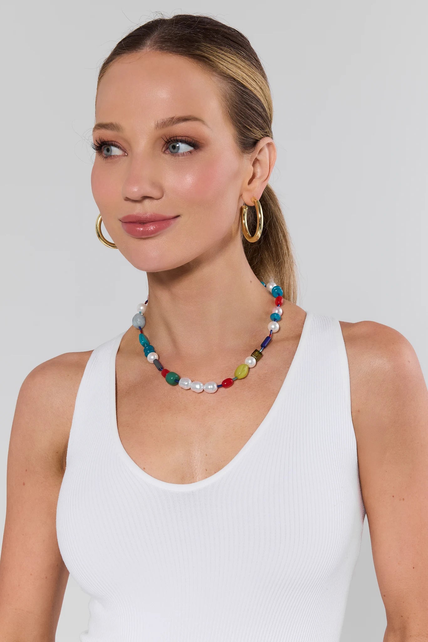 Woman wearing a colorful beaded necklace and hoop earrings on a plain background