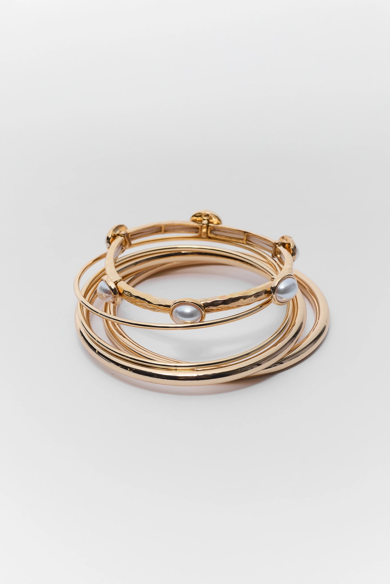 close up Set of gold bracelets with pearl accents on a light gray background