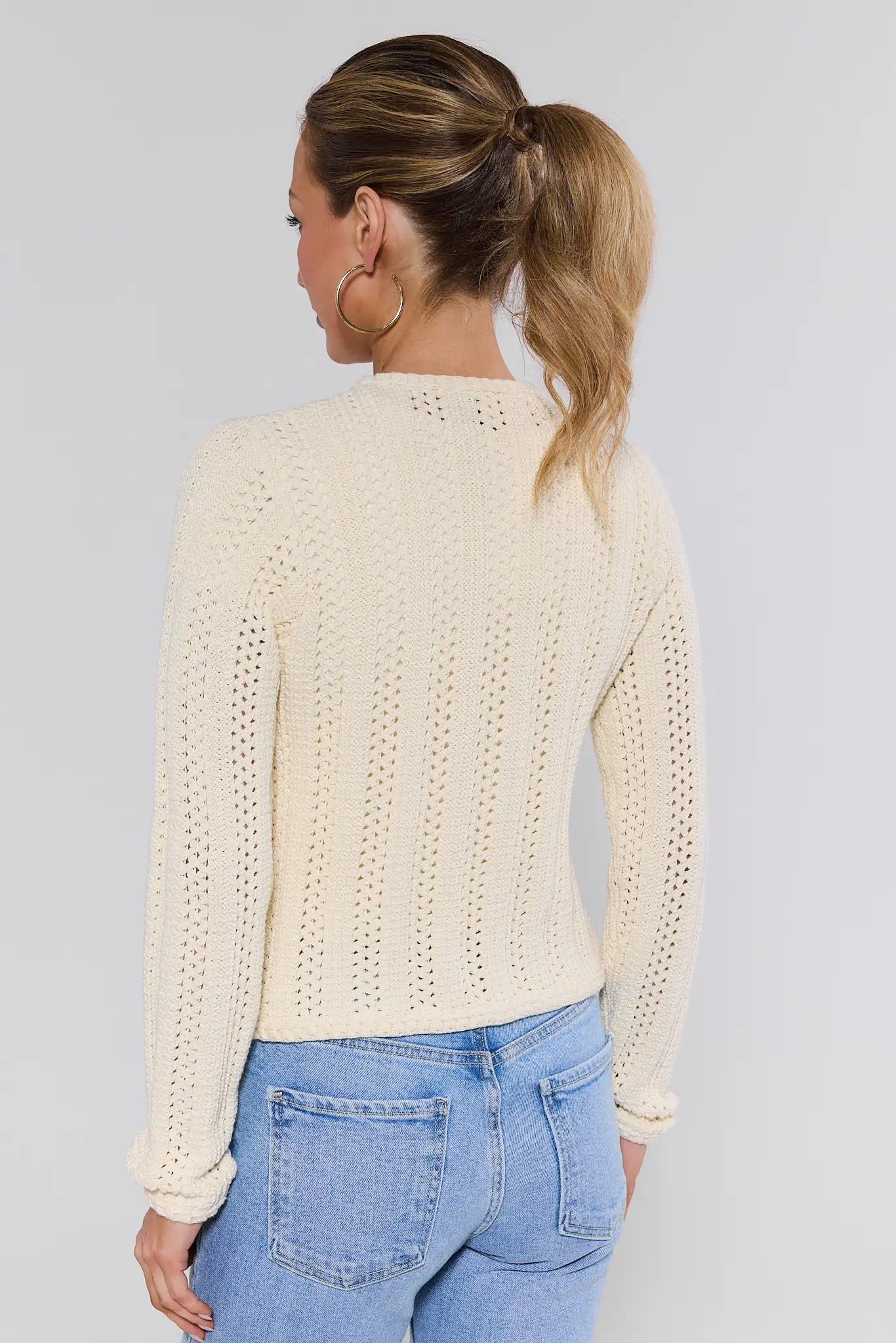 Woman wearing a cream knitted sweater and blue jeans on a plain background