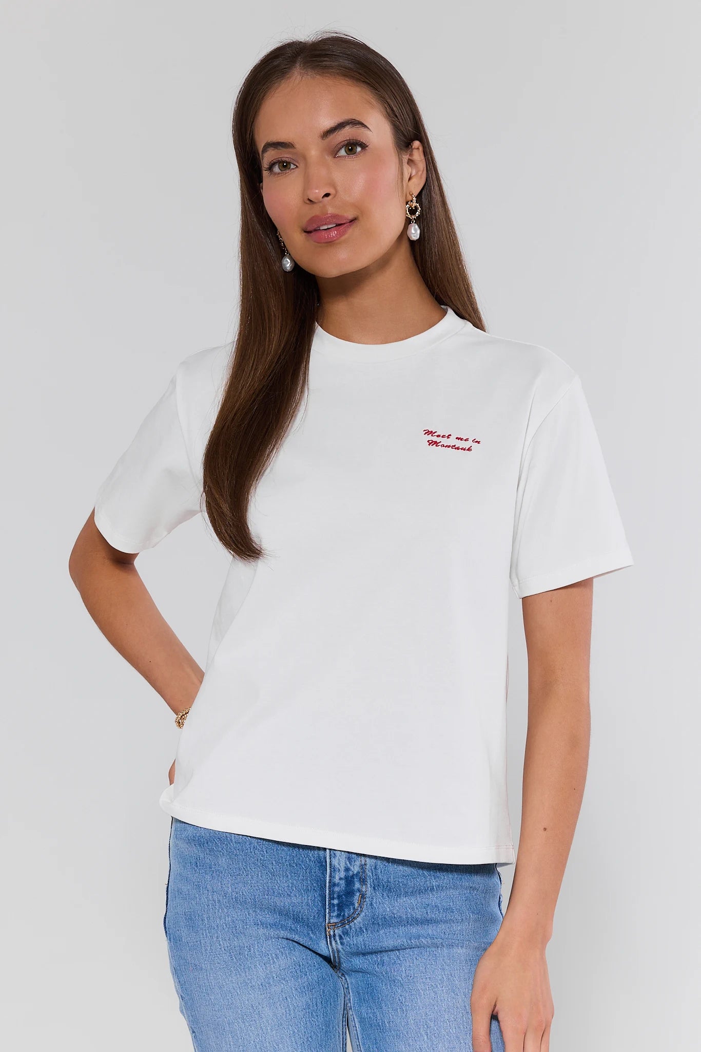 Woman wearing a white t-shirt with red text and blue jeans on a plain background