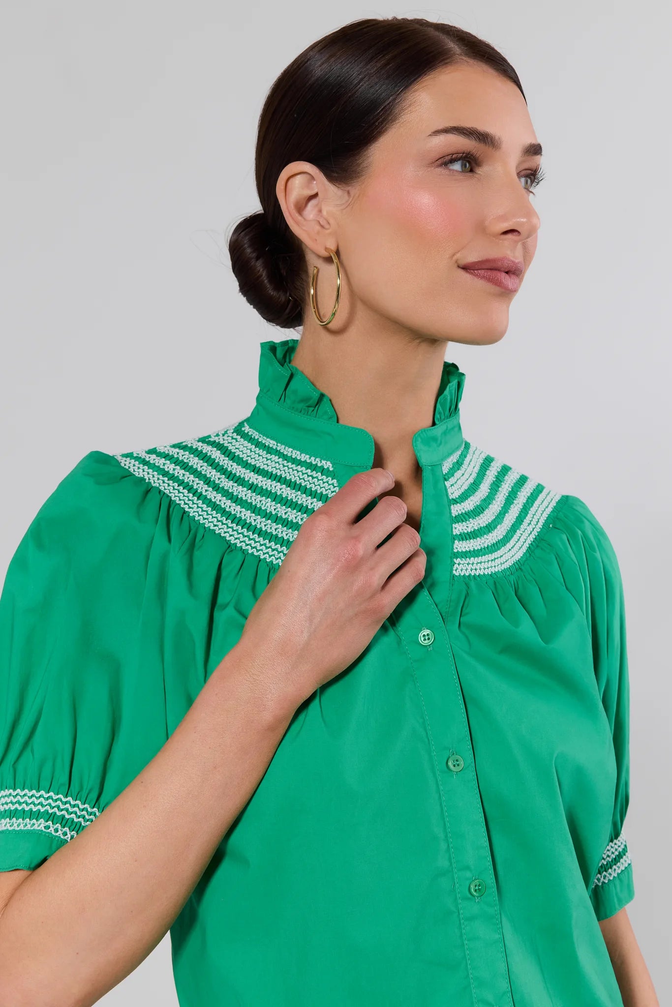 close up Woman wearing a green blouse with white embroidery against a plain background