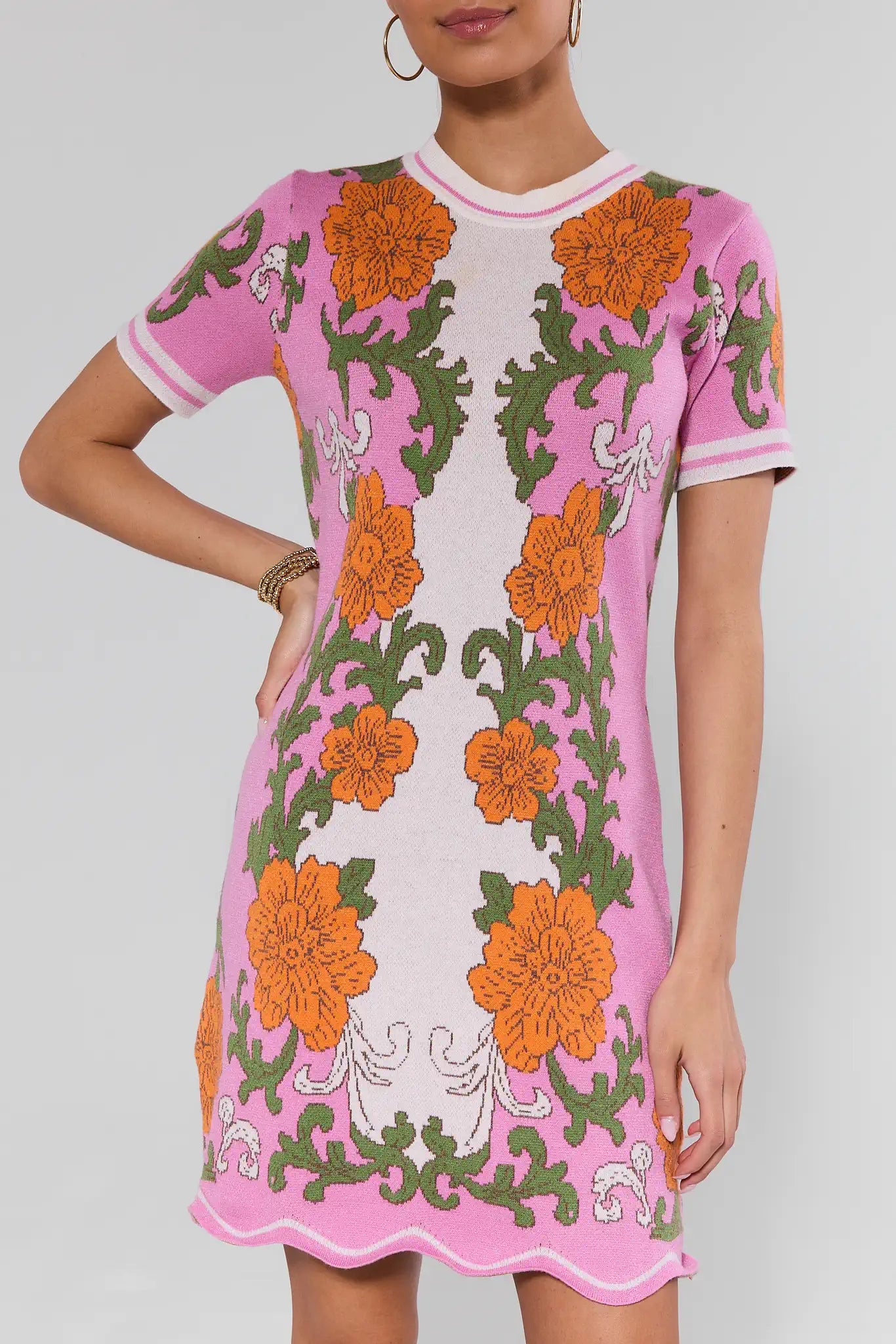 Pink dress with orange and green floral patterns worn by a model on a gray background