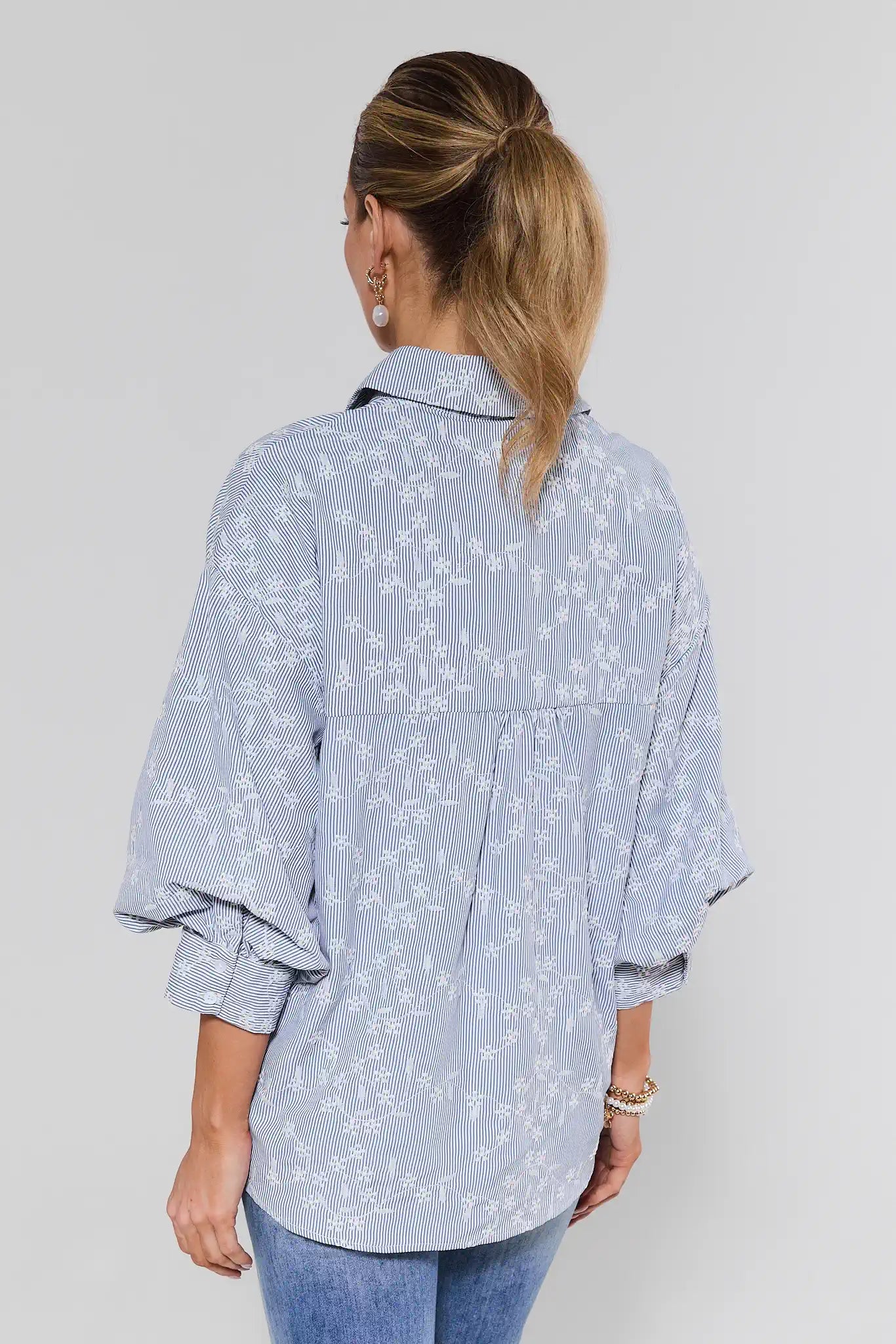 Woman wearing a light blue floral blouse with rolled-up sleeves on a white background