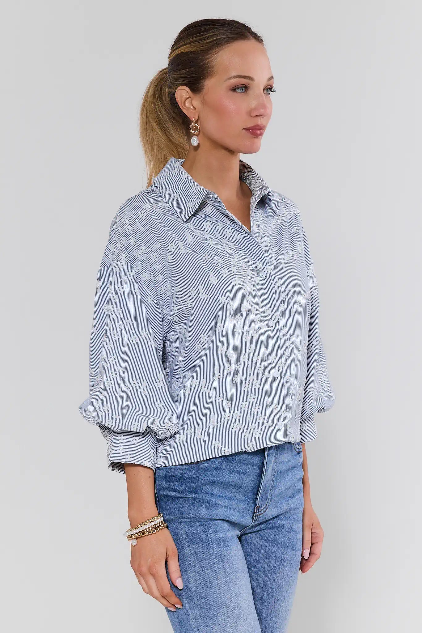 Woman wearing a light blue floral blouse and jeans against a background