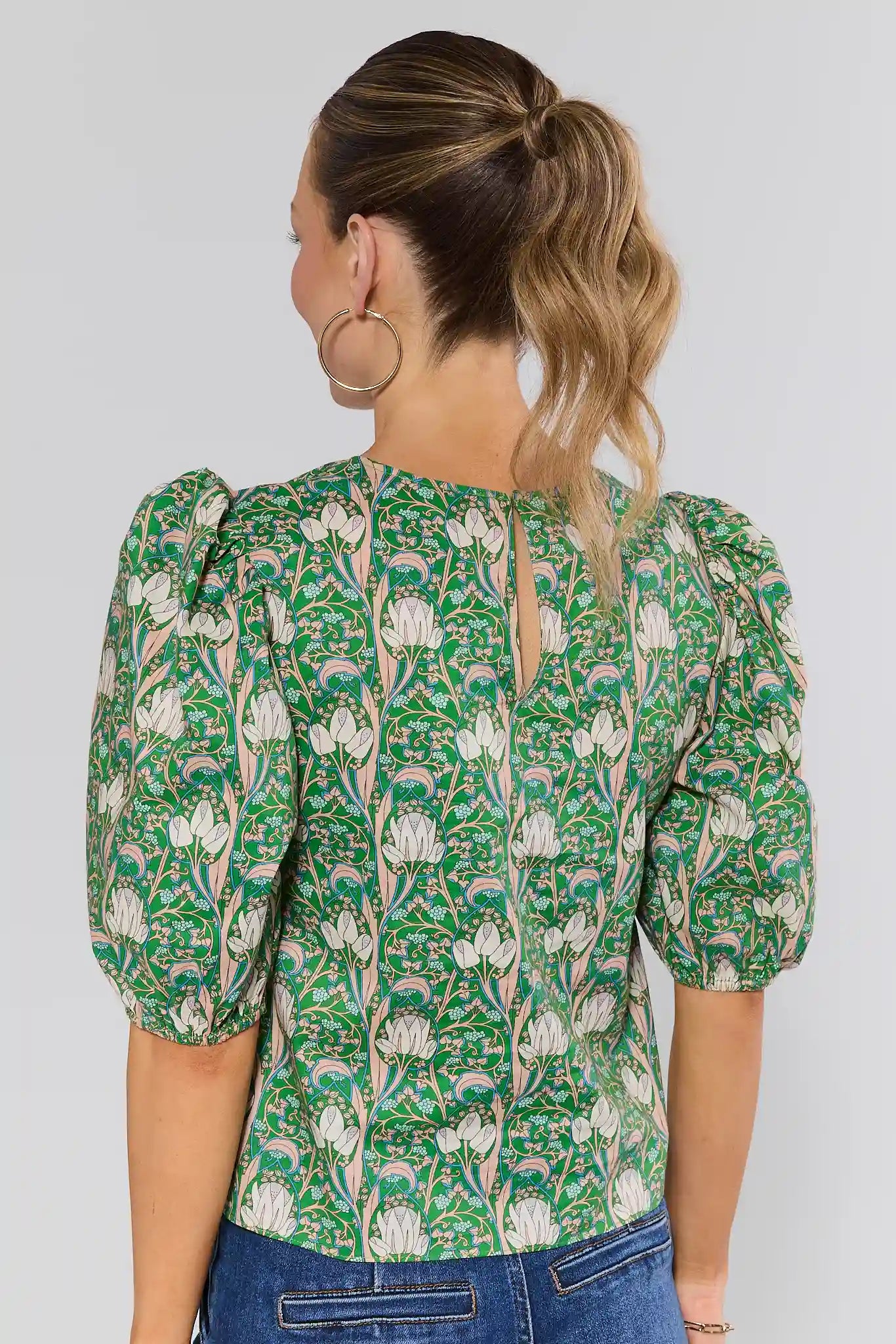 Woman standing wearing a green floral blouse with puffed sleeves on a plain background