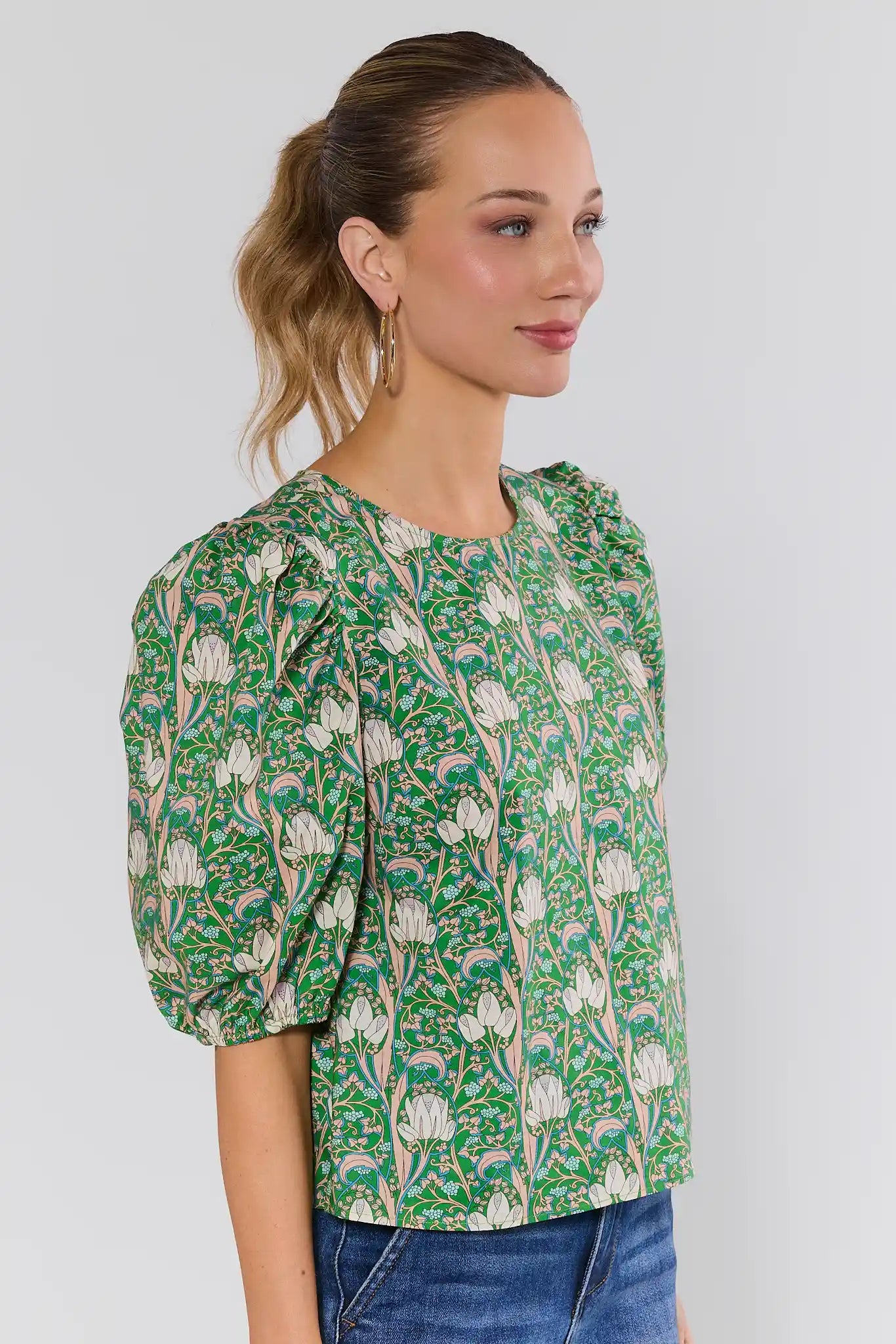 Woman side shot wearing a green floral blouse against a plain background