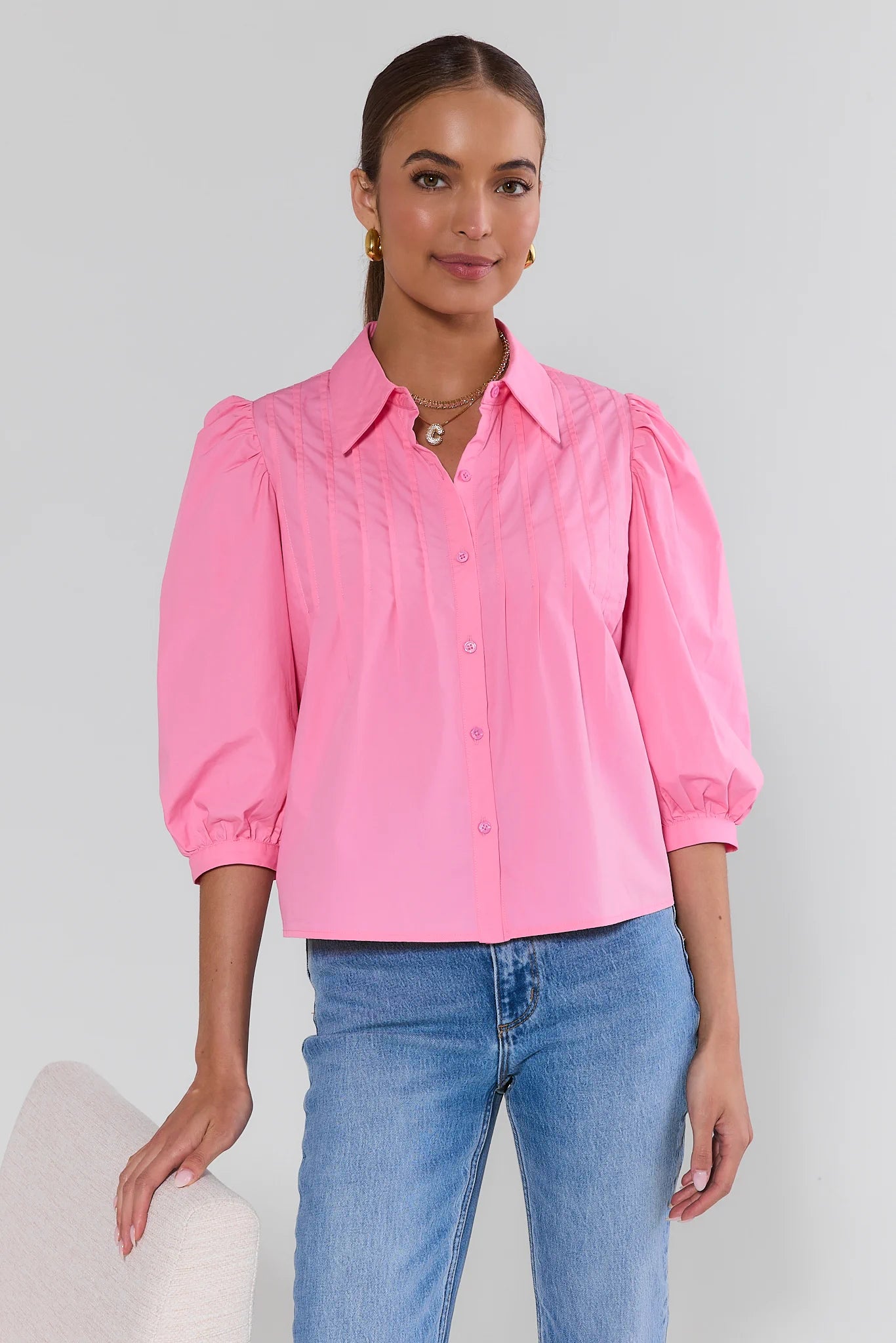 Woman wearing a pink blouse and blue jeans against a plain background