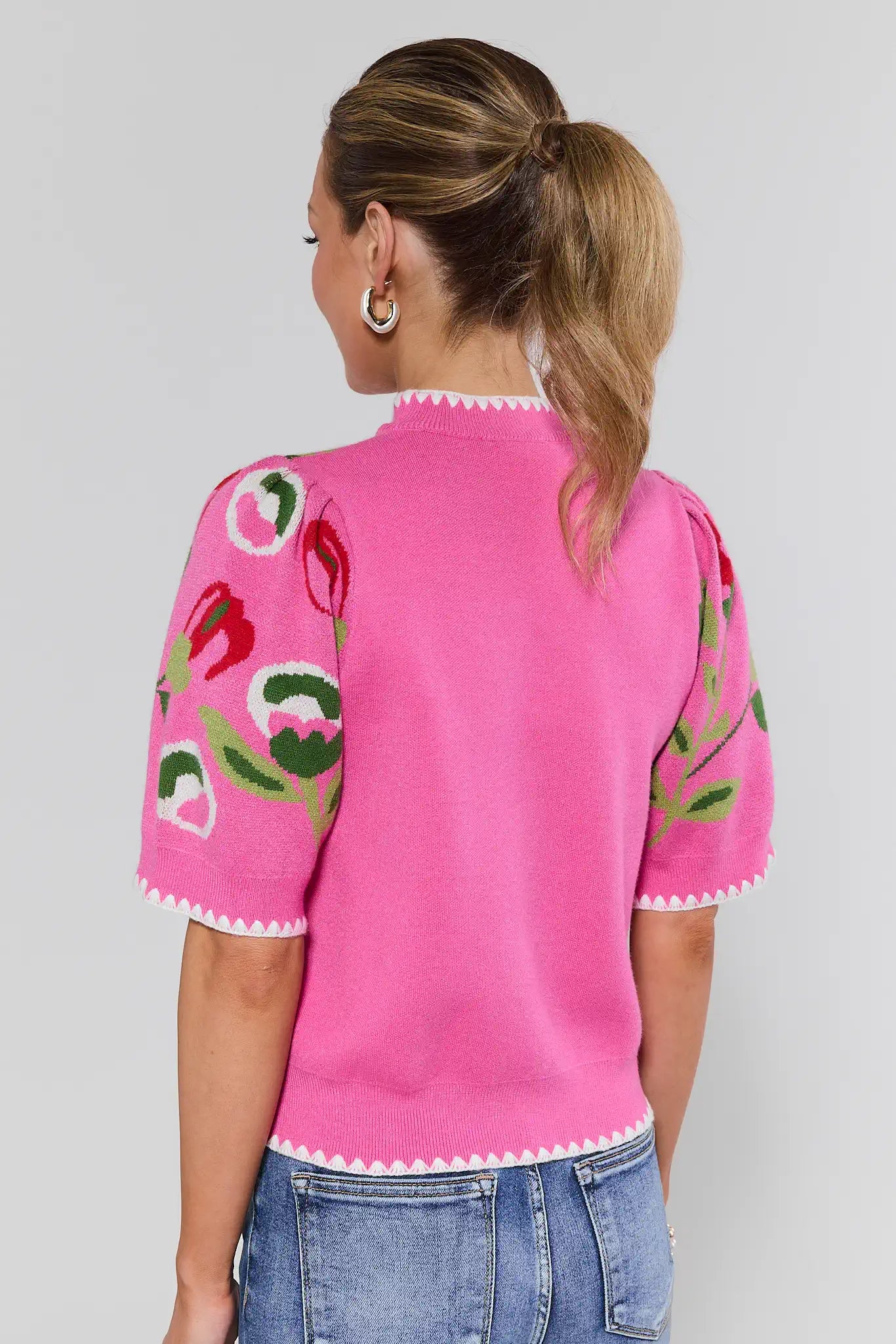 Person wearing a pink sweater with floral patterns on a plain background