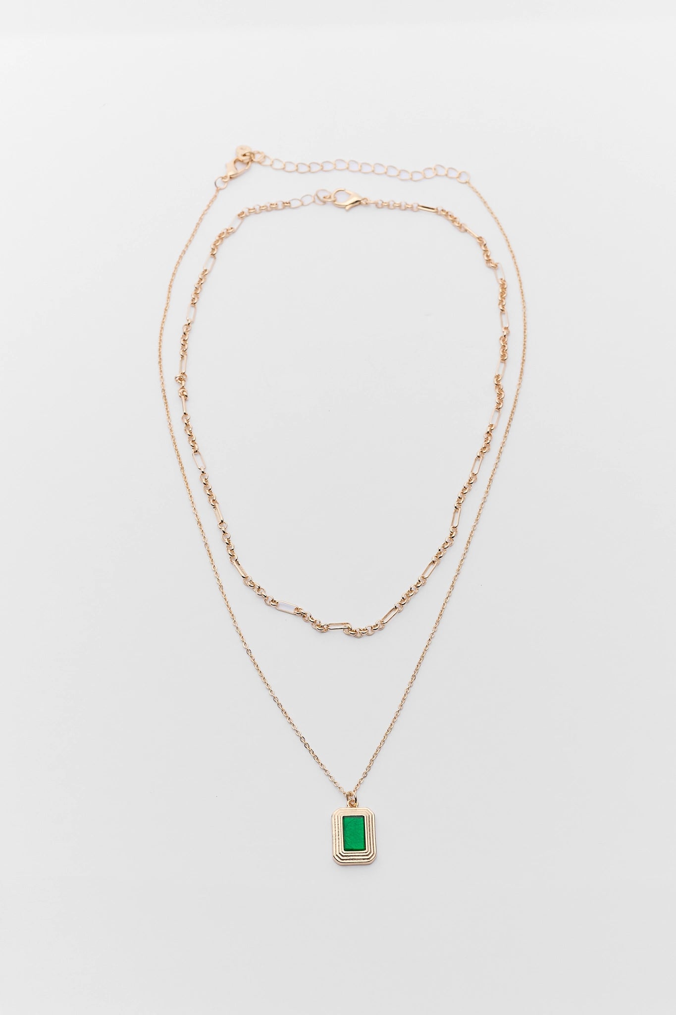 Two gold necklaces with a green pendant on a light gray background