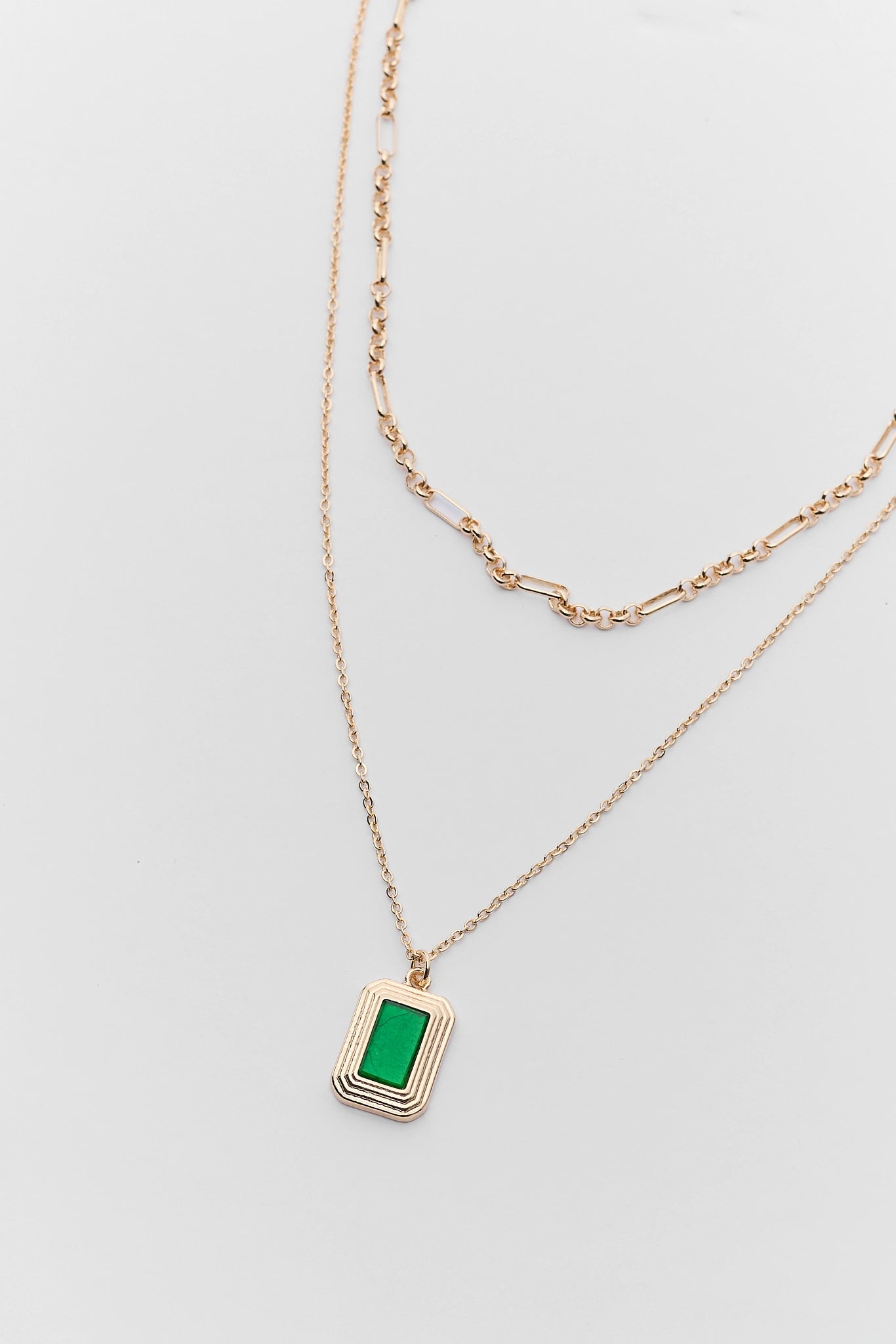 Gold necklace with a green pendant on a light gray background