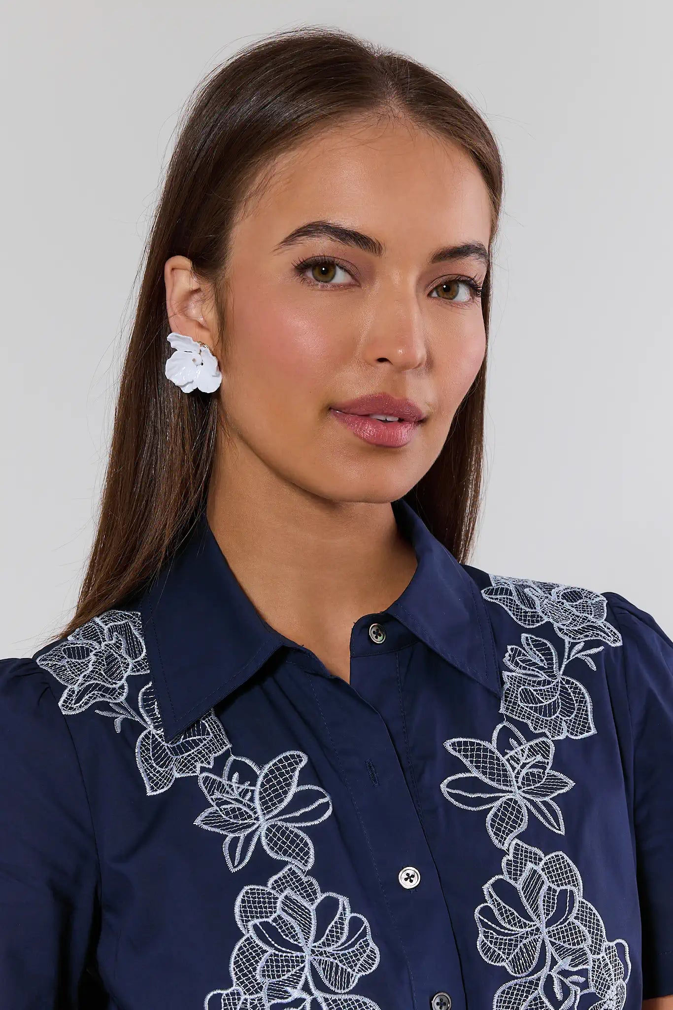 Woman wearing a navy blue shirt with white floral embroidery on a plain background