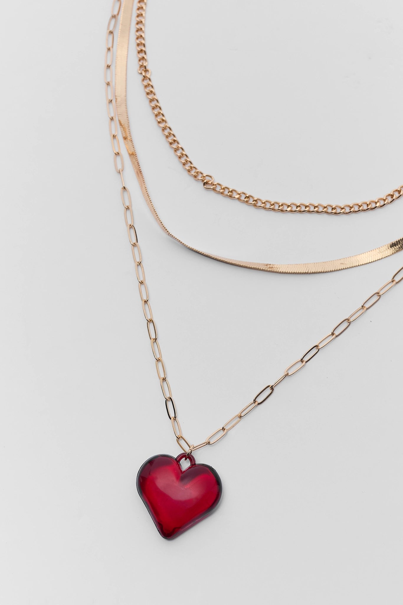 Two gold necklaces with red heart pendants on a light gray background