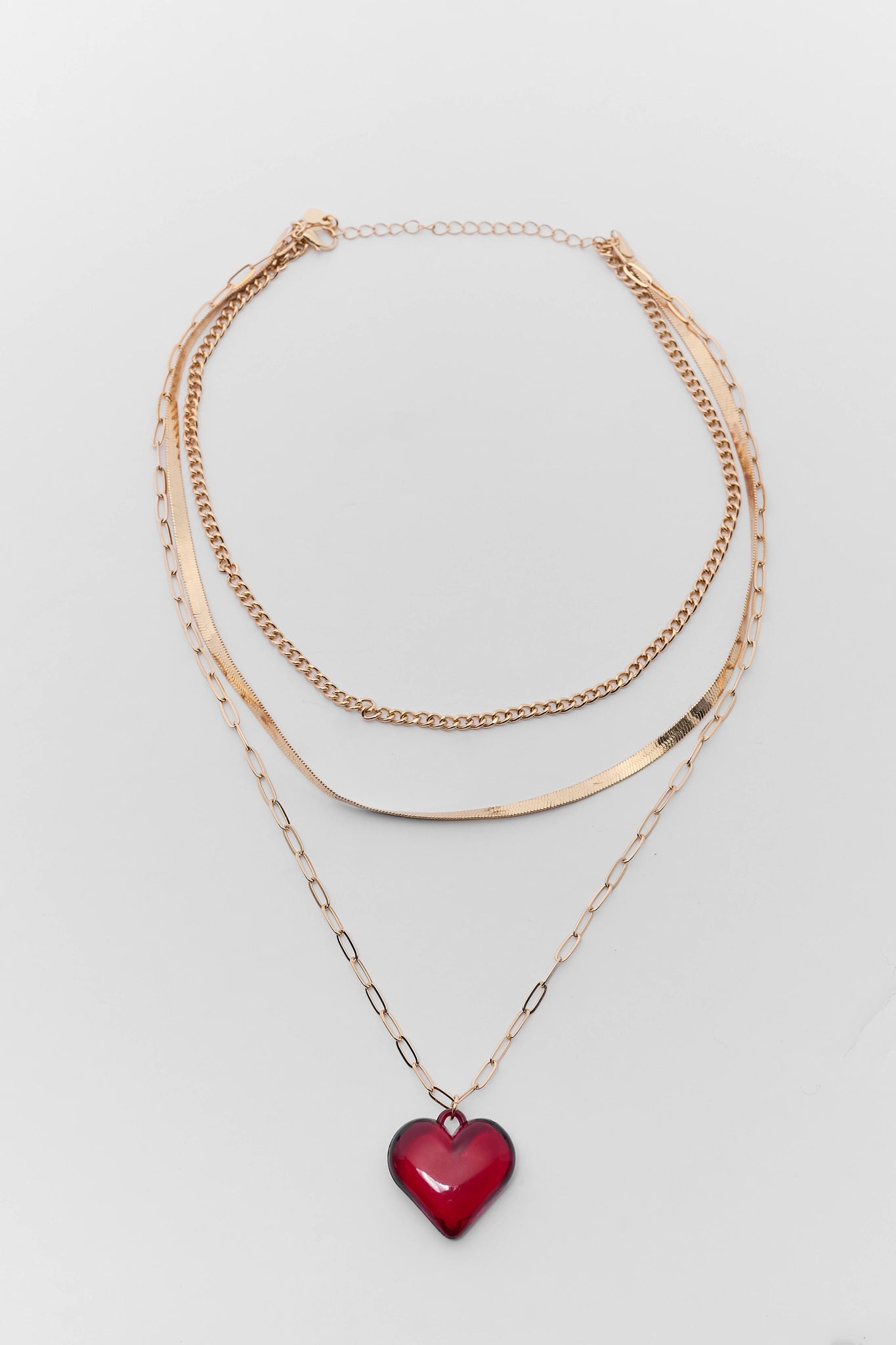 Three gold necklaces with a red heart pendant on a light gray background