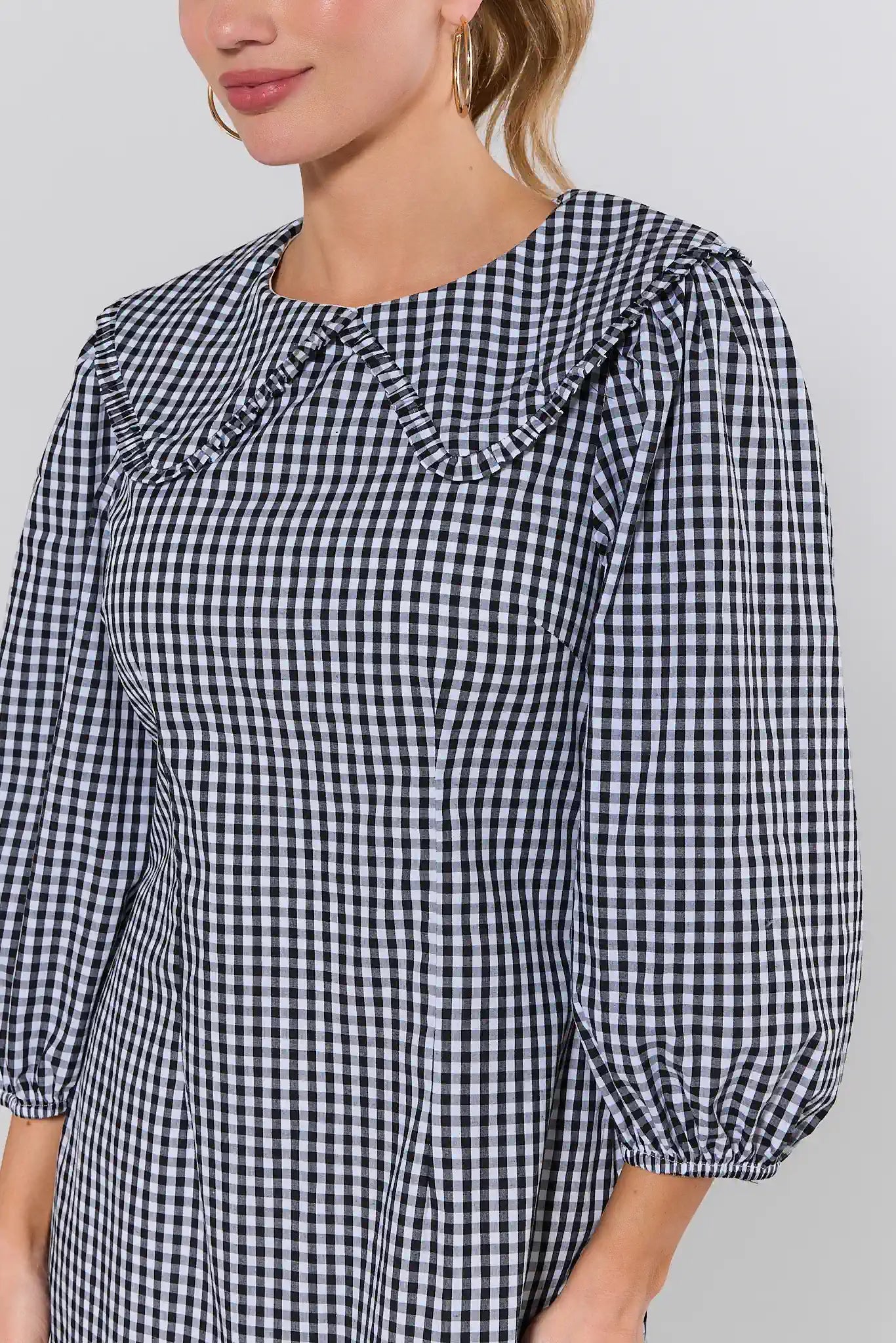 Woman wearing a black and white checkered blouse with ruffled neckline on a gray background