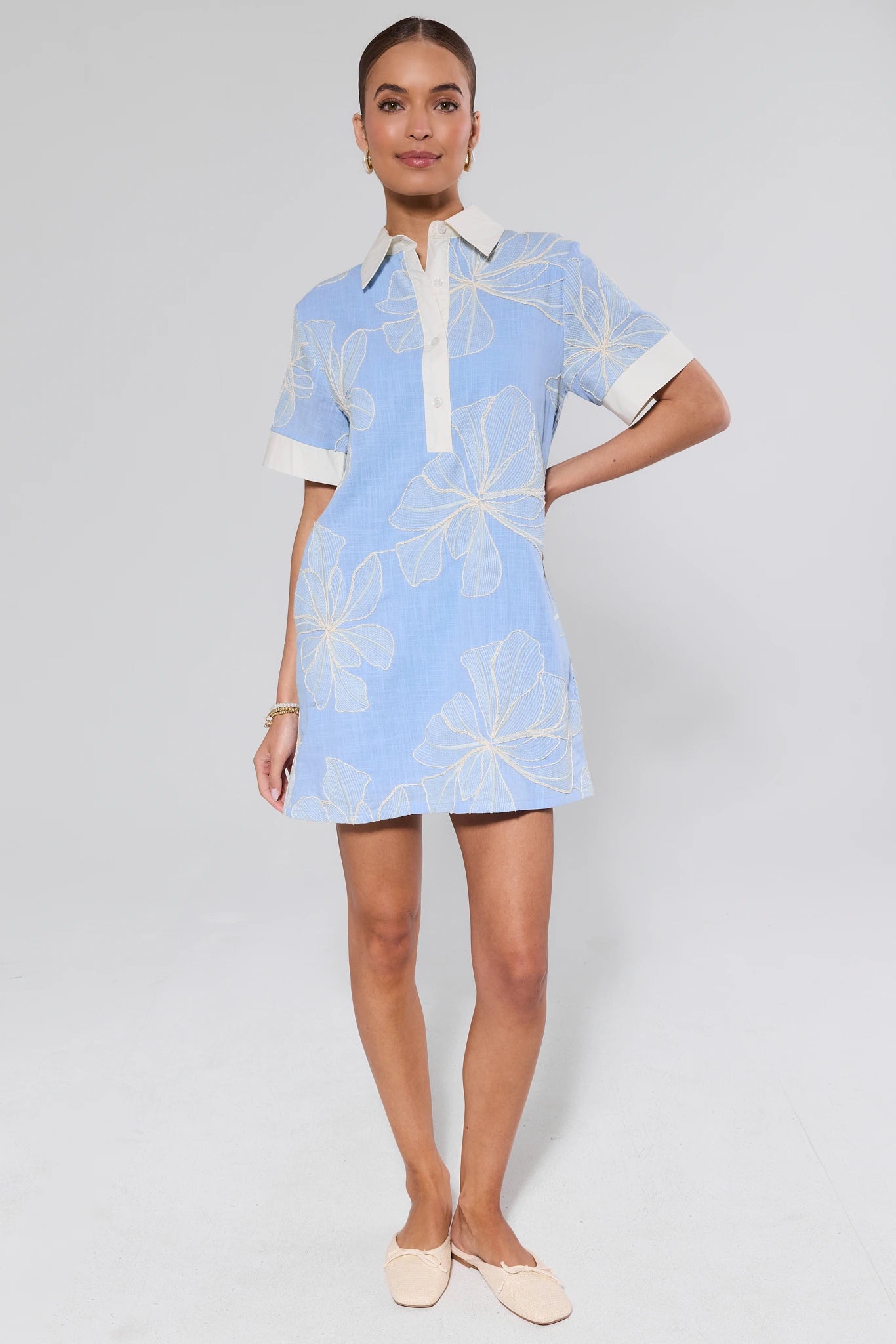 Woman wearing a light blue dress with white floral patterns on a plain background