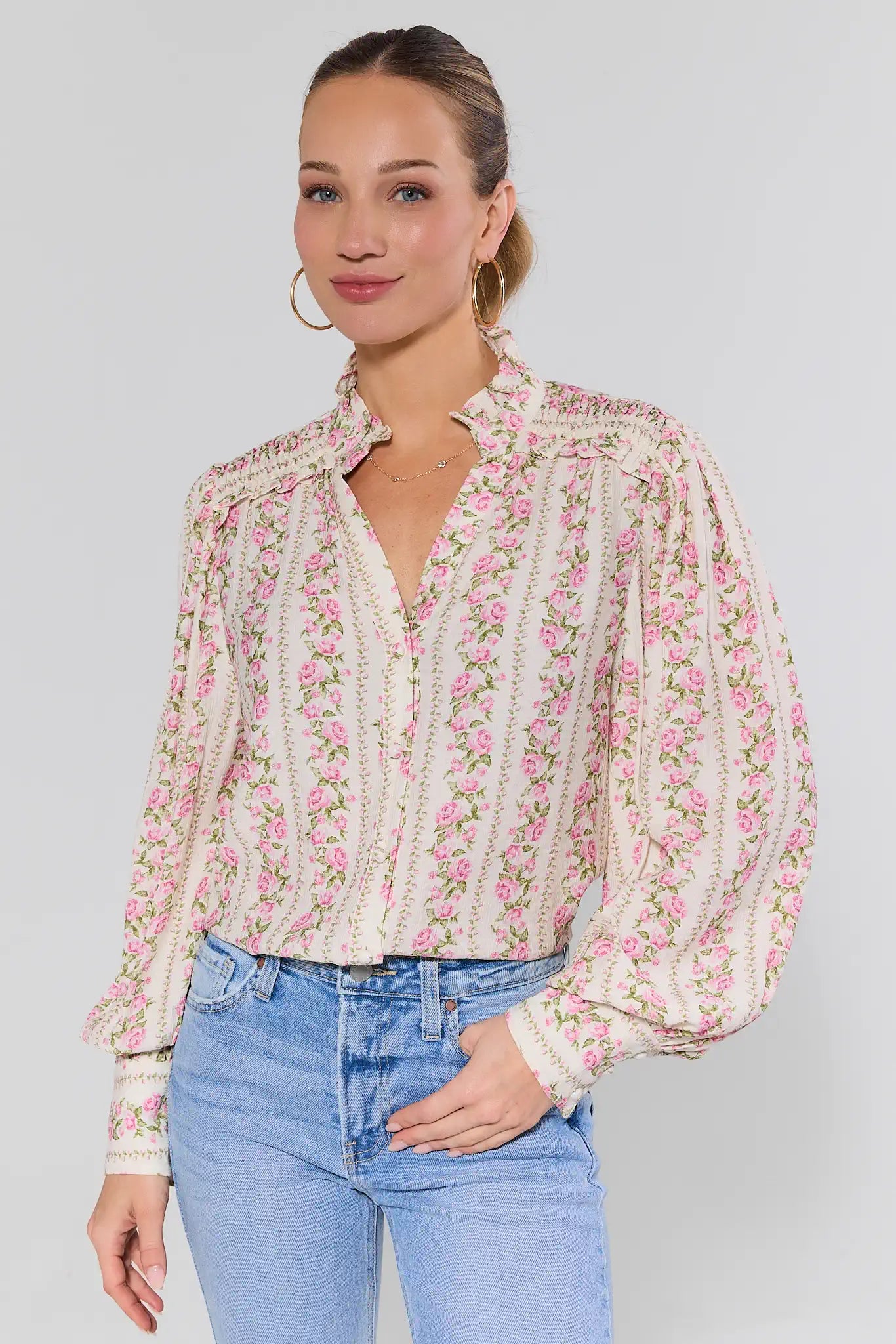 Woman wearing a floral blouse and blue jeans against a plain background