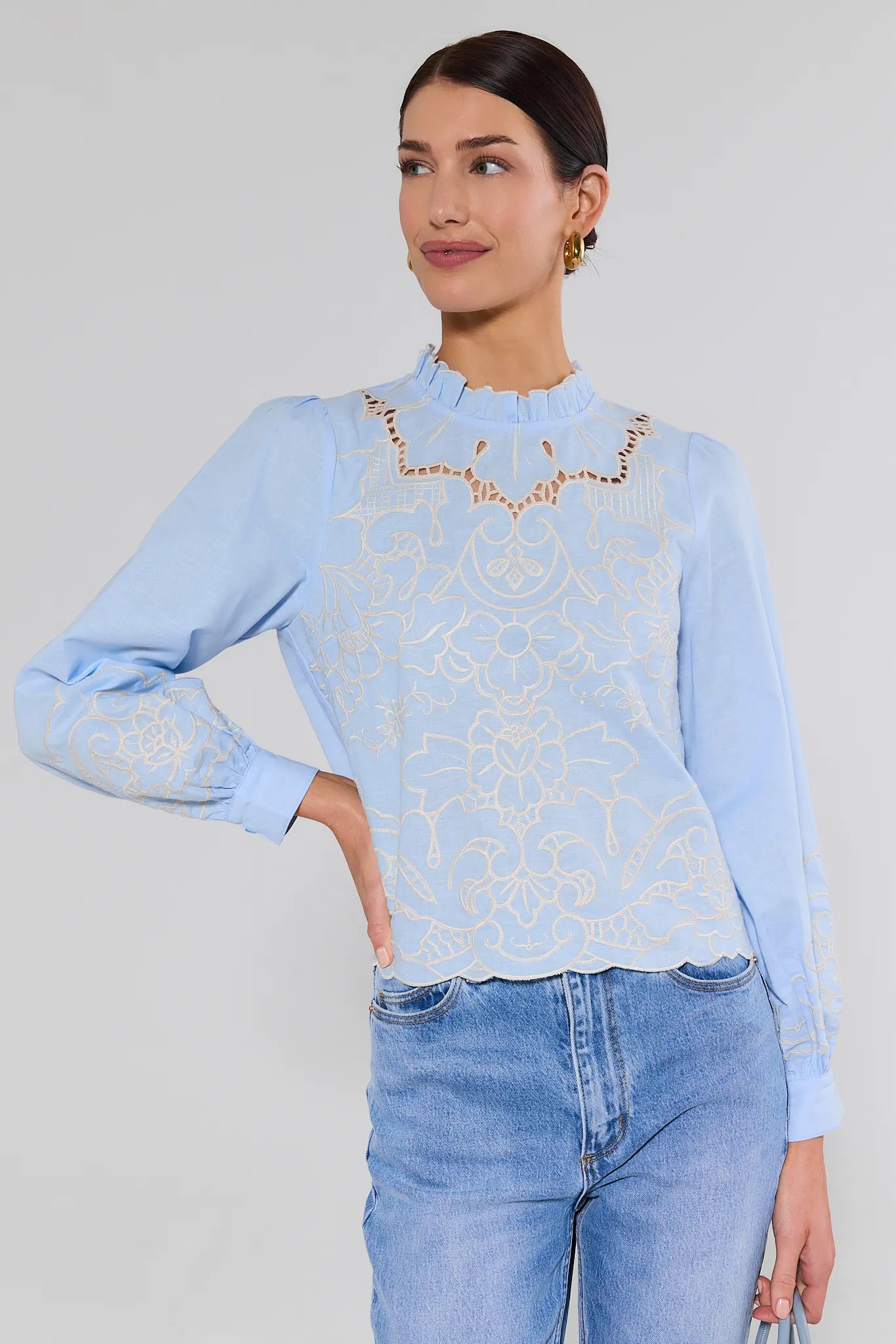 Woman wearing a light blue blouse with lace details and jeans on a plain background