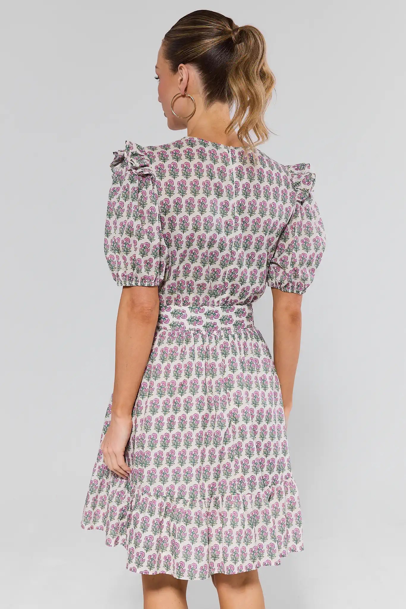 Woman standing wearing a floral dress with puff sleeves on a plain background