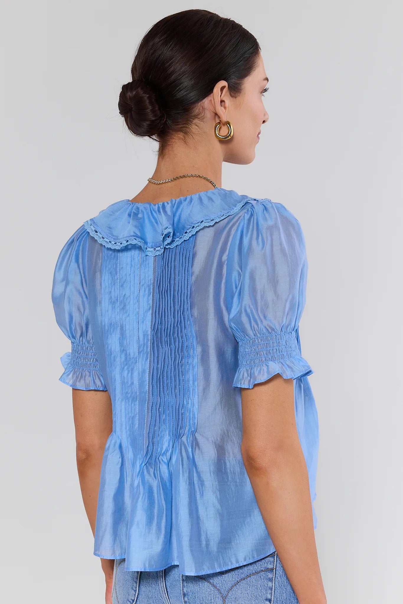 Woman wearing a light blouse with puffed sleeves on a plain background