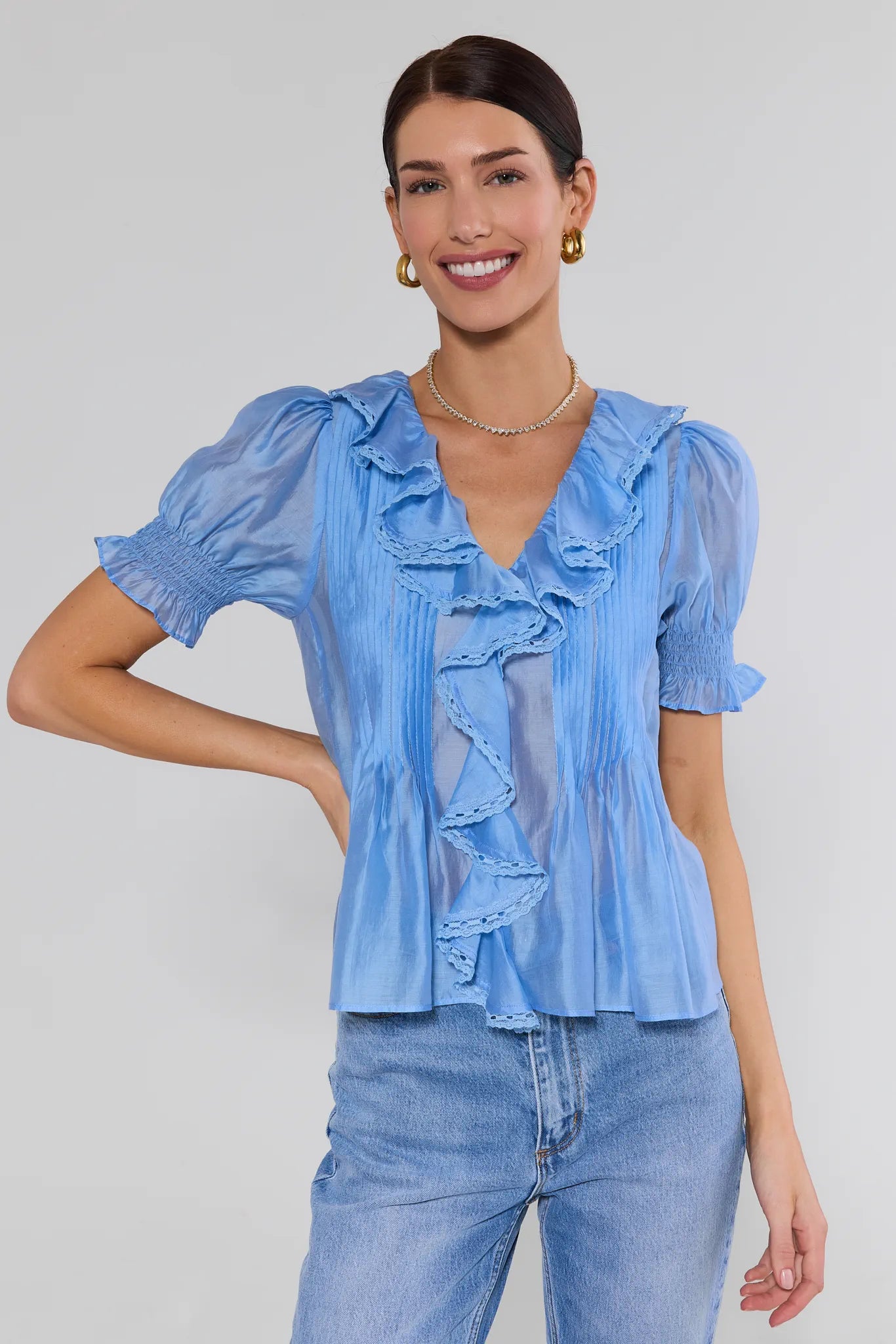 Woman wearing a blue ruffled blouse and blue jeans against a plain background