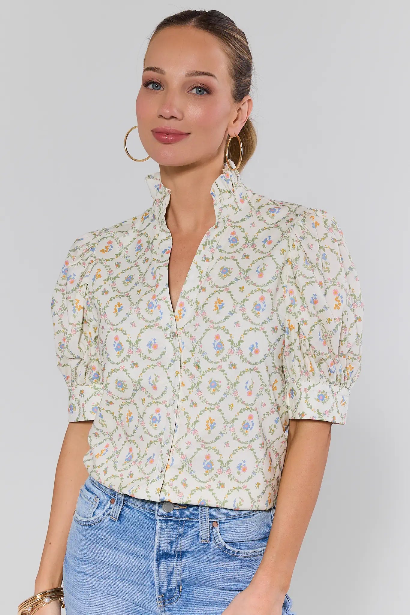 Woman wearing a floral blouse and blue jeans against a plain background