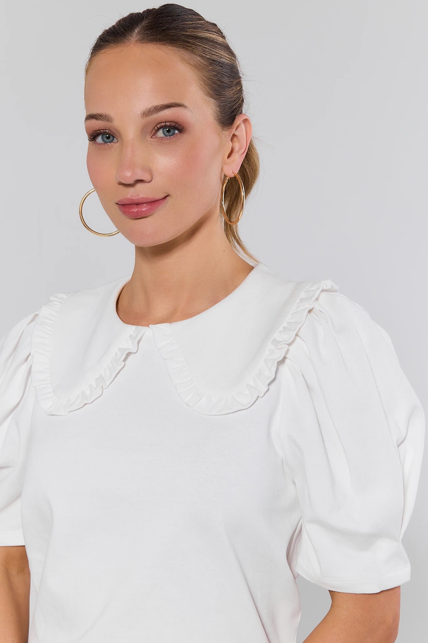 close up Woman wearing a white blouse with puffed sleeves against a plain background