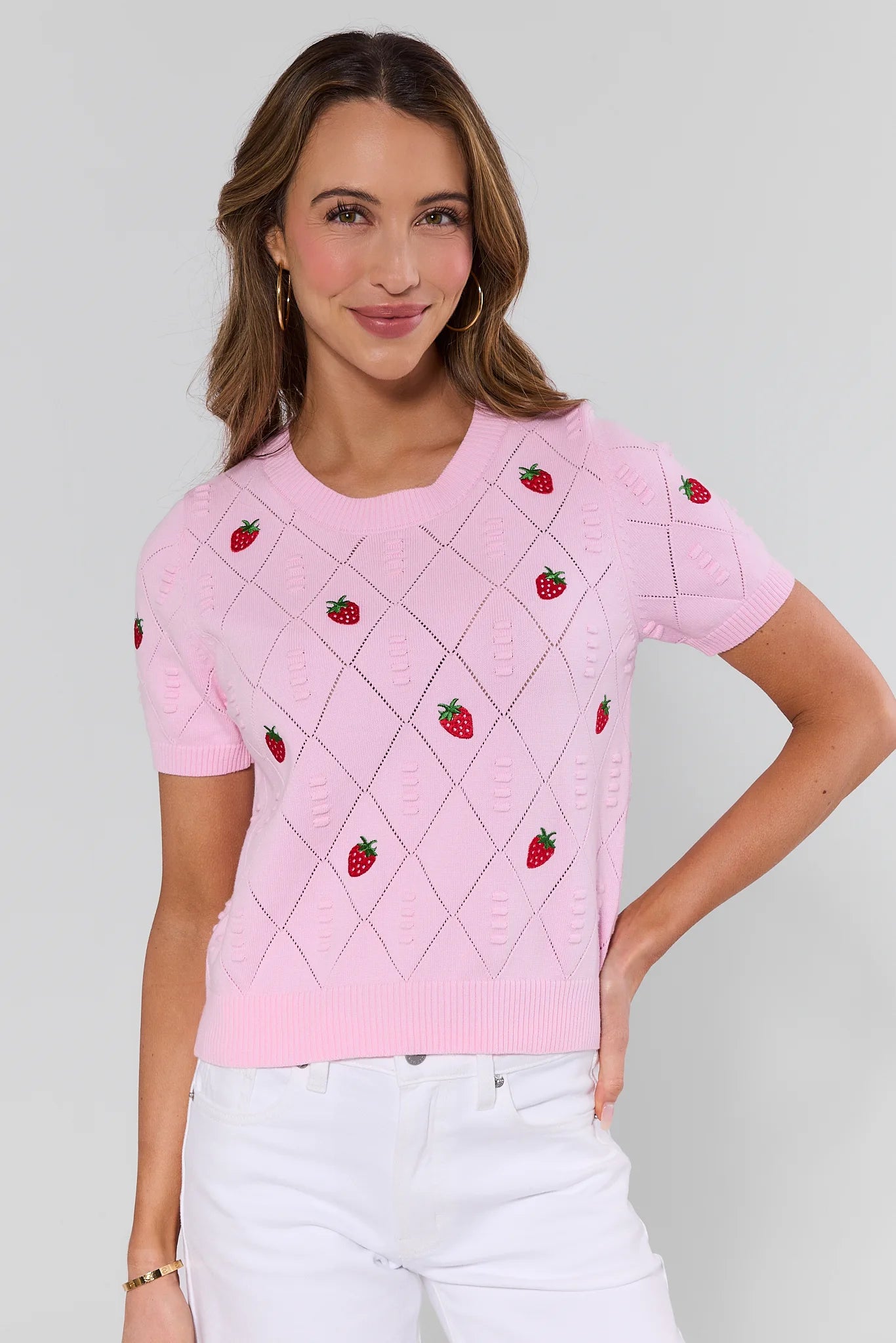 Woman wearing a pink sweater with strawberry patterns on a plain background
