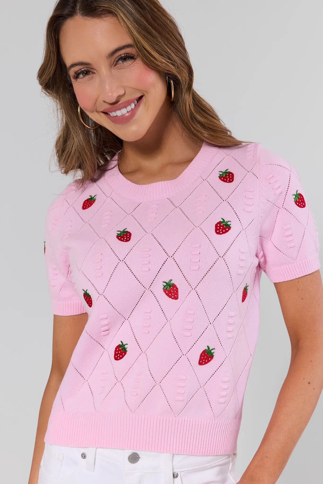 Woman wearing a pink sweater with strawberry patterns on a plain background
