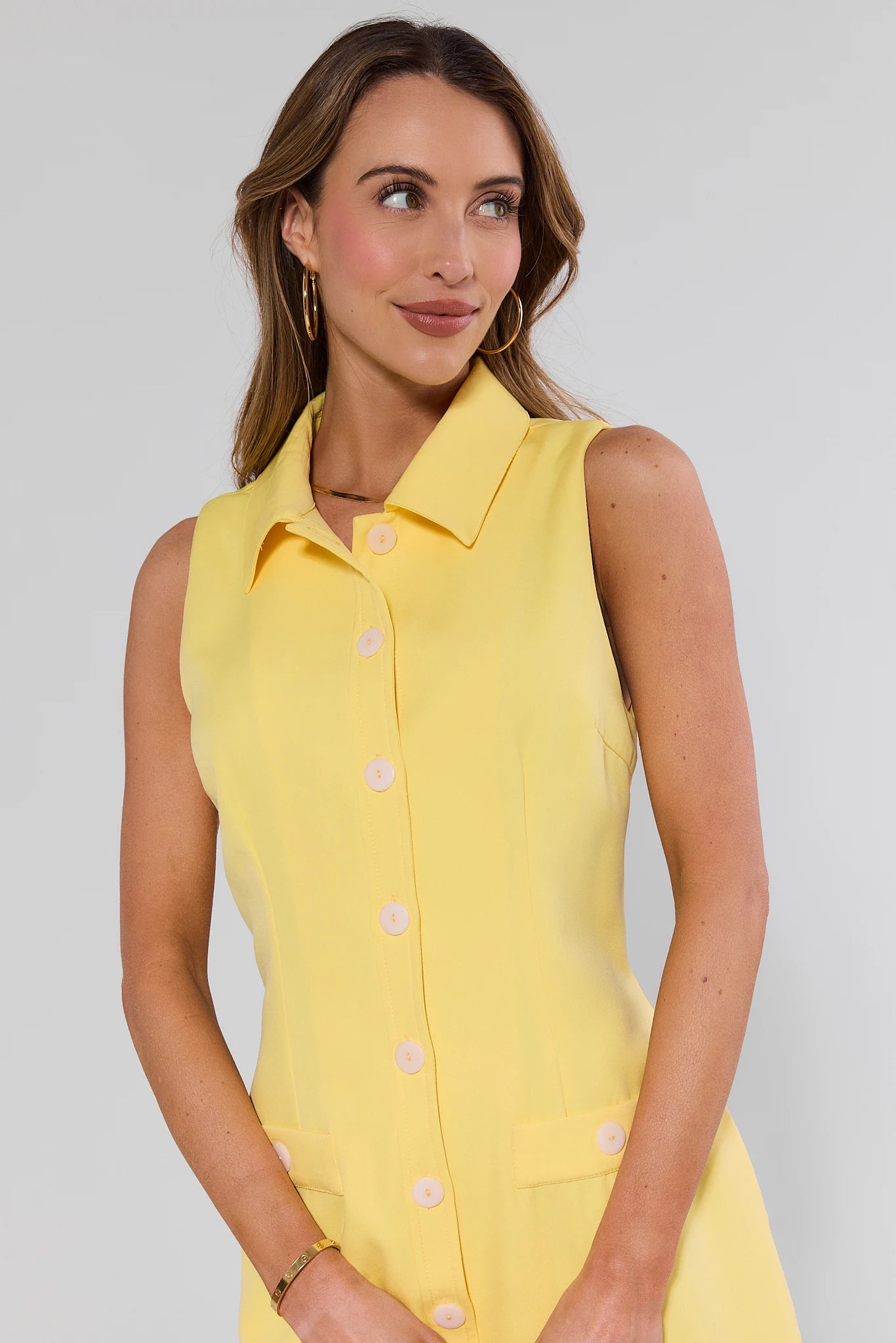 close up Woman wearing a yellow sleeveless dress with buttons on a plain background