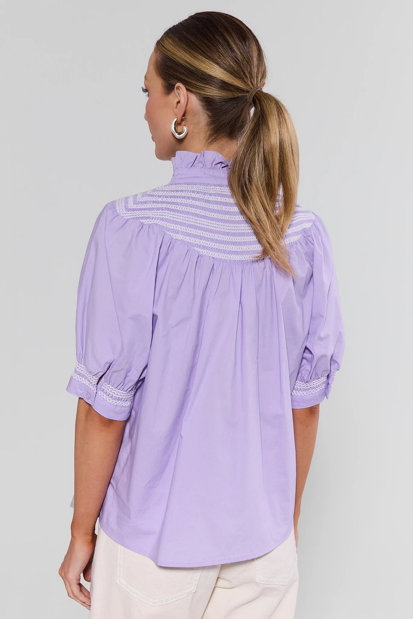 Woman wearing a light purple blouse with a subtle pattern on a plain background