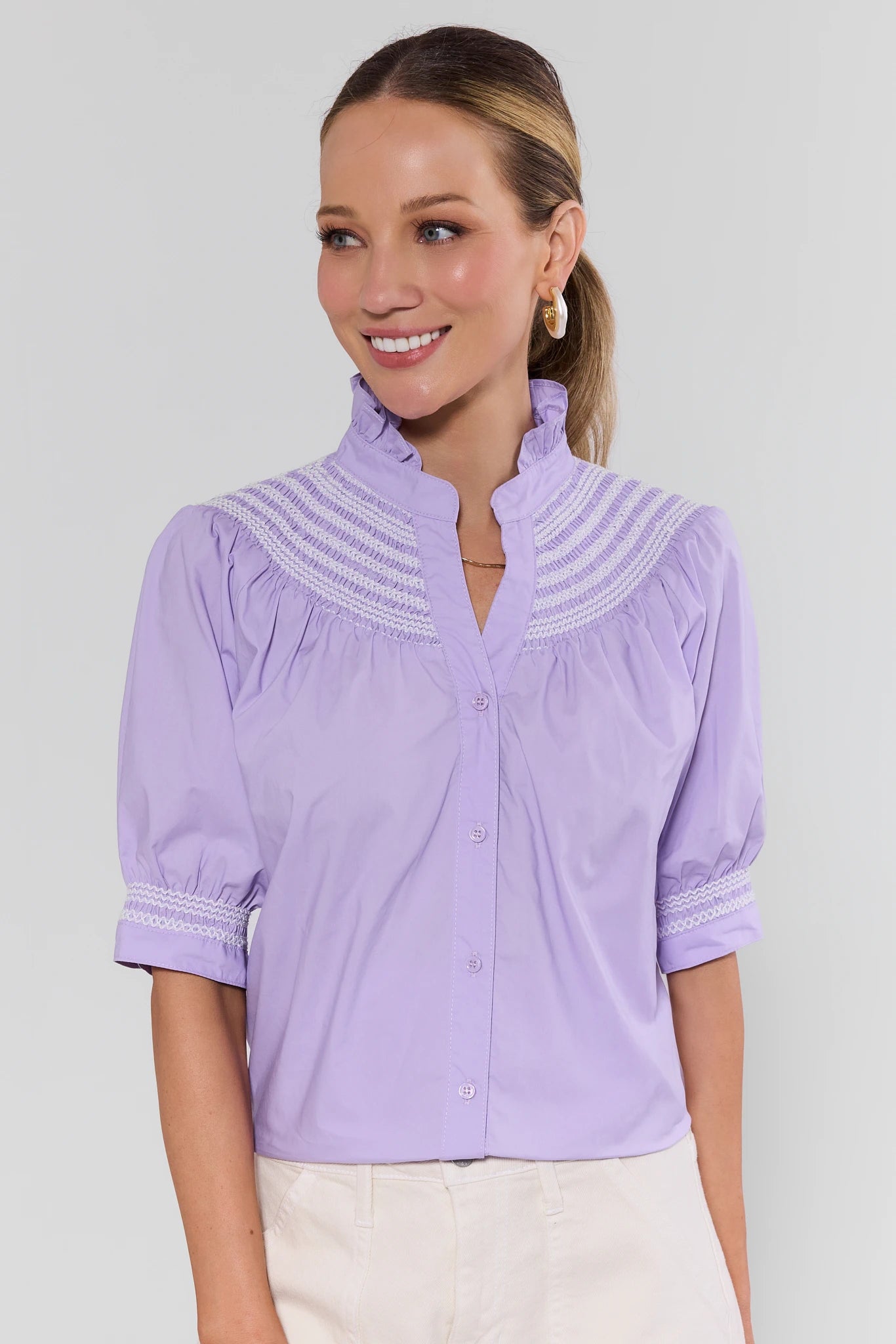 Woman wearing a light purple blouse with lace details on a plain background