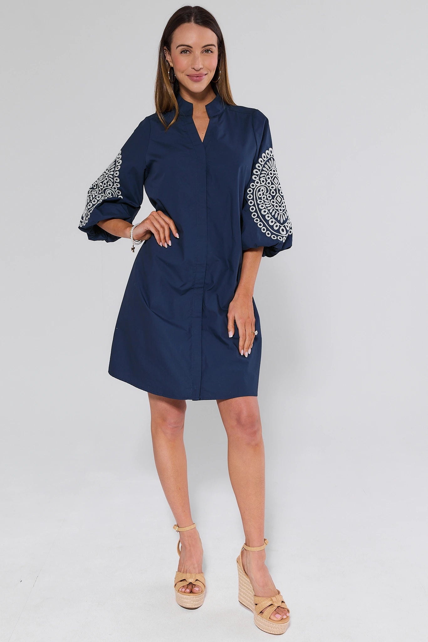 Woman wearing a navy dress with white embroidery on sleeves against a white background