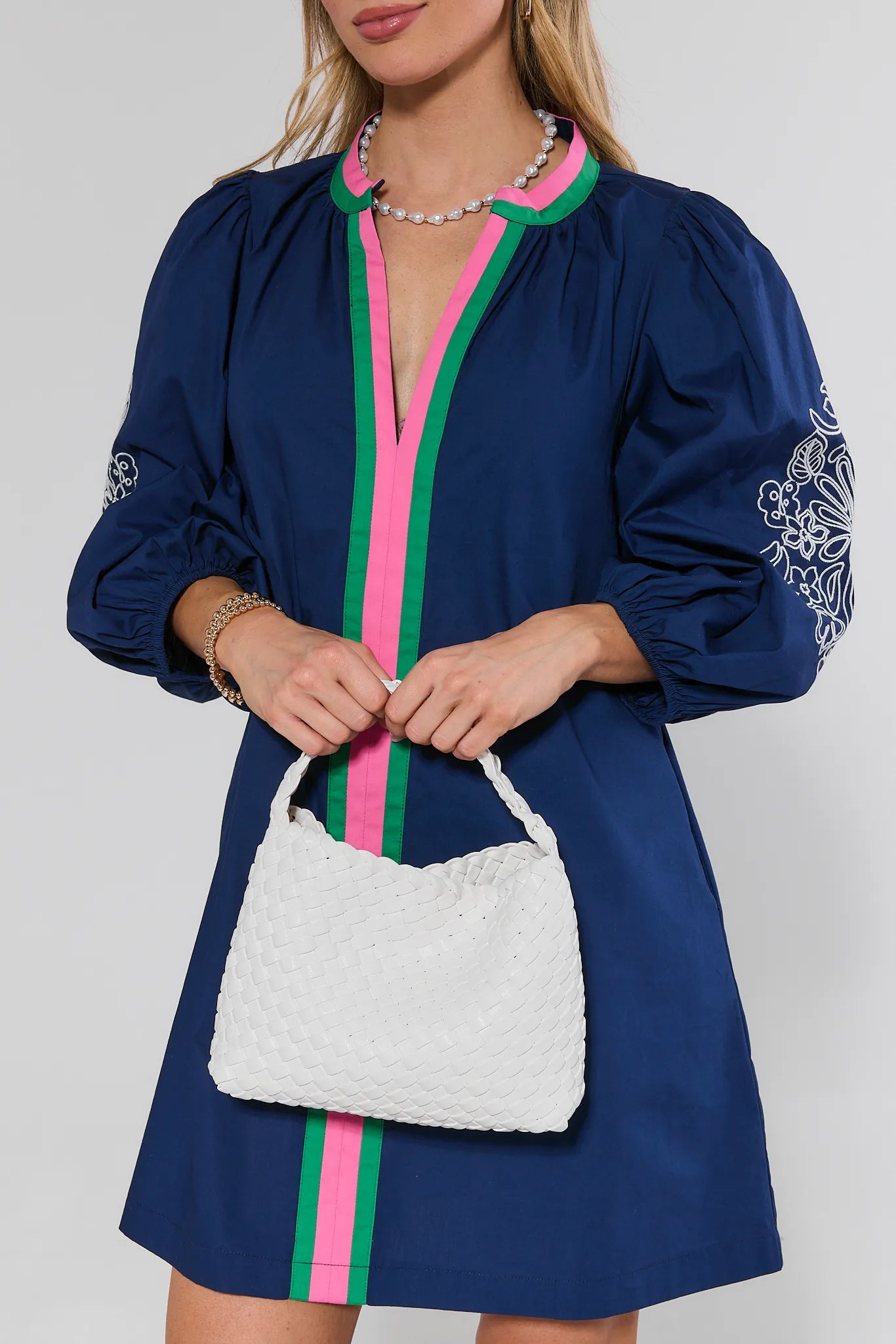 Woman wearing a blue dress with pink and green accents, holding a white textured handbag.