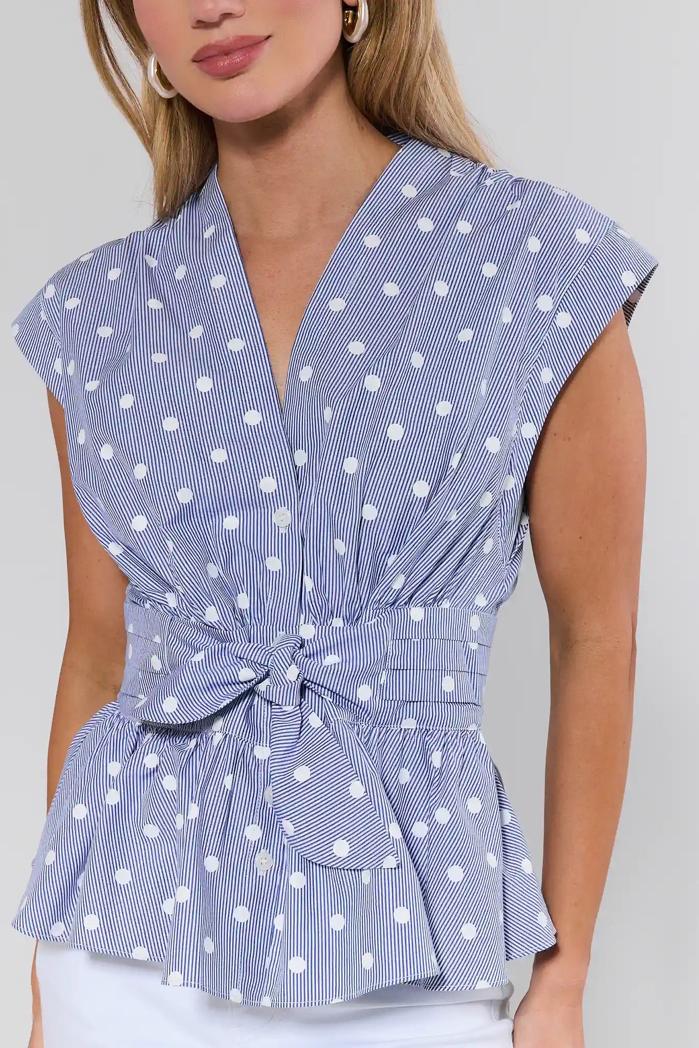 Woman wearing a blue and white polka dot top with a tie waist on a plain background