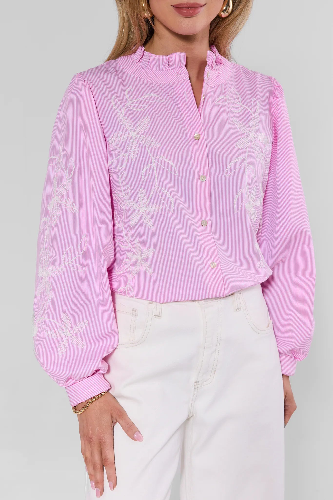 Woman wearing a pink floral blouse with white pants on a plain background