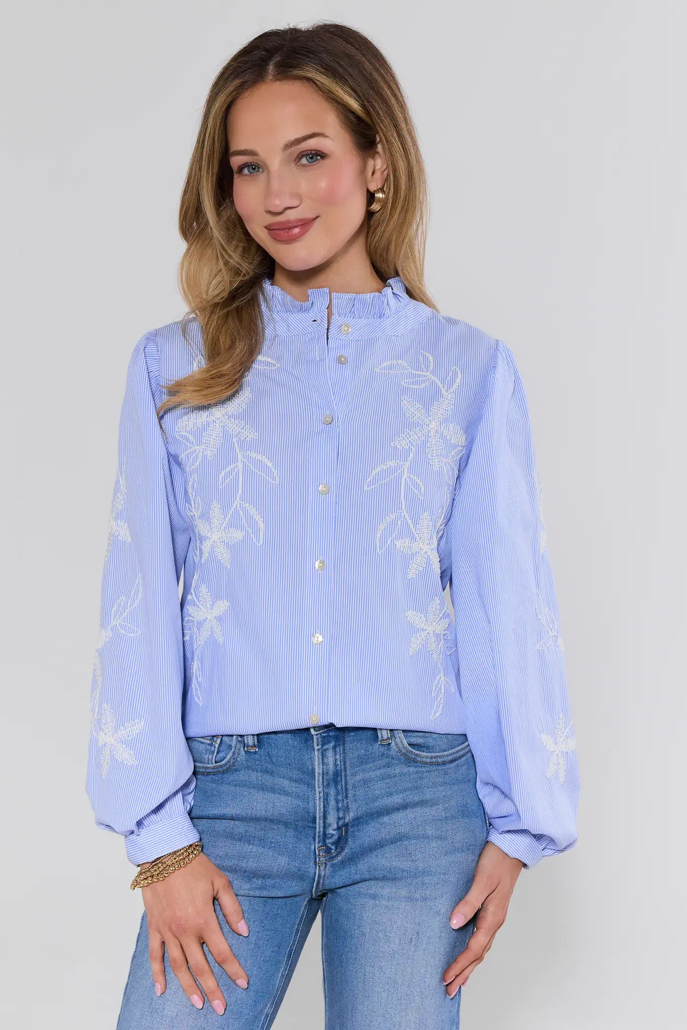 Woman wearing a light blue blouse with floral patterns and jeans on a plain background