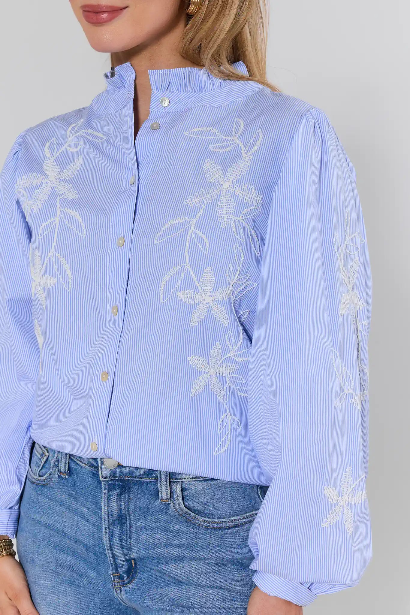 Light blue blouse with white floral embroidery worn by a person, against a plain background