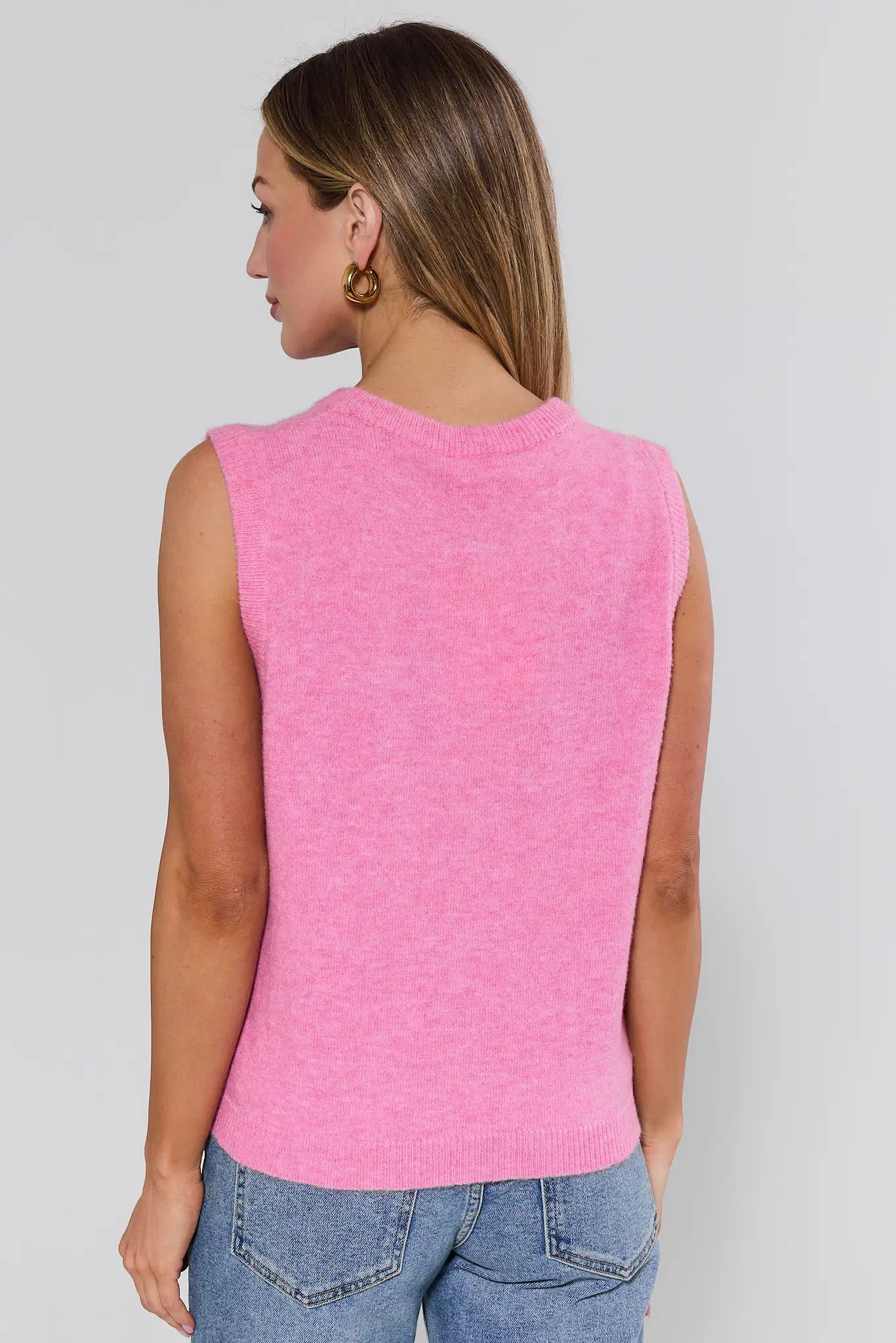 Person wearing a pink sleeveless sweater against a plain background