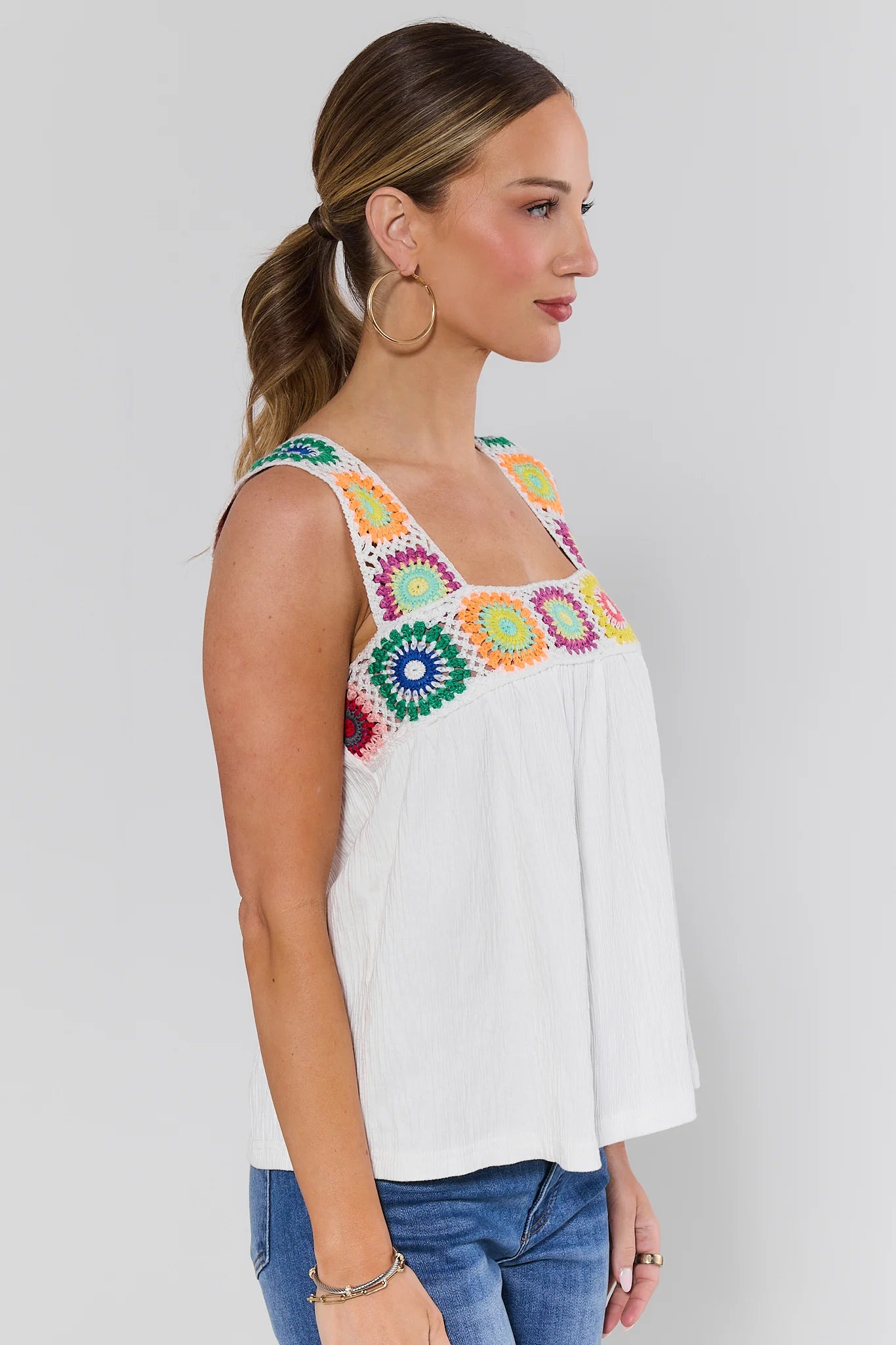 Woman wearing a white sleeveless top with colorful floral embroidery on a background