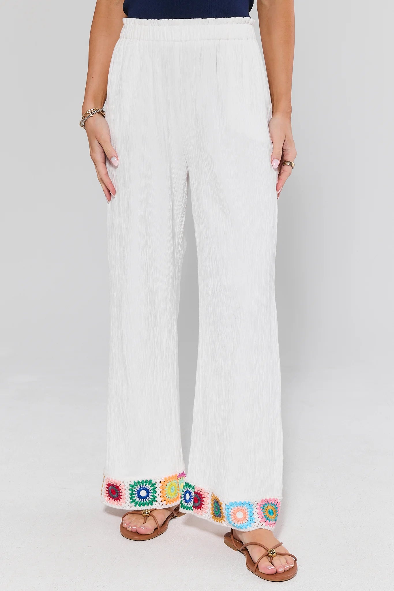 White poppy pants with colorful embroidery at the bottom worn by a person on a white background