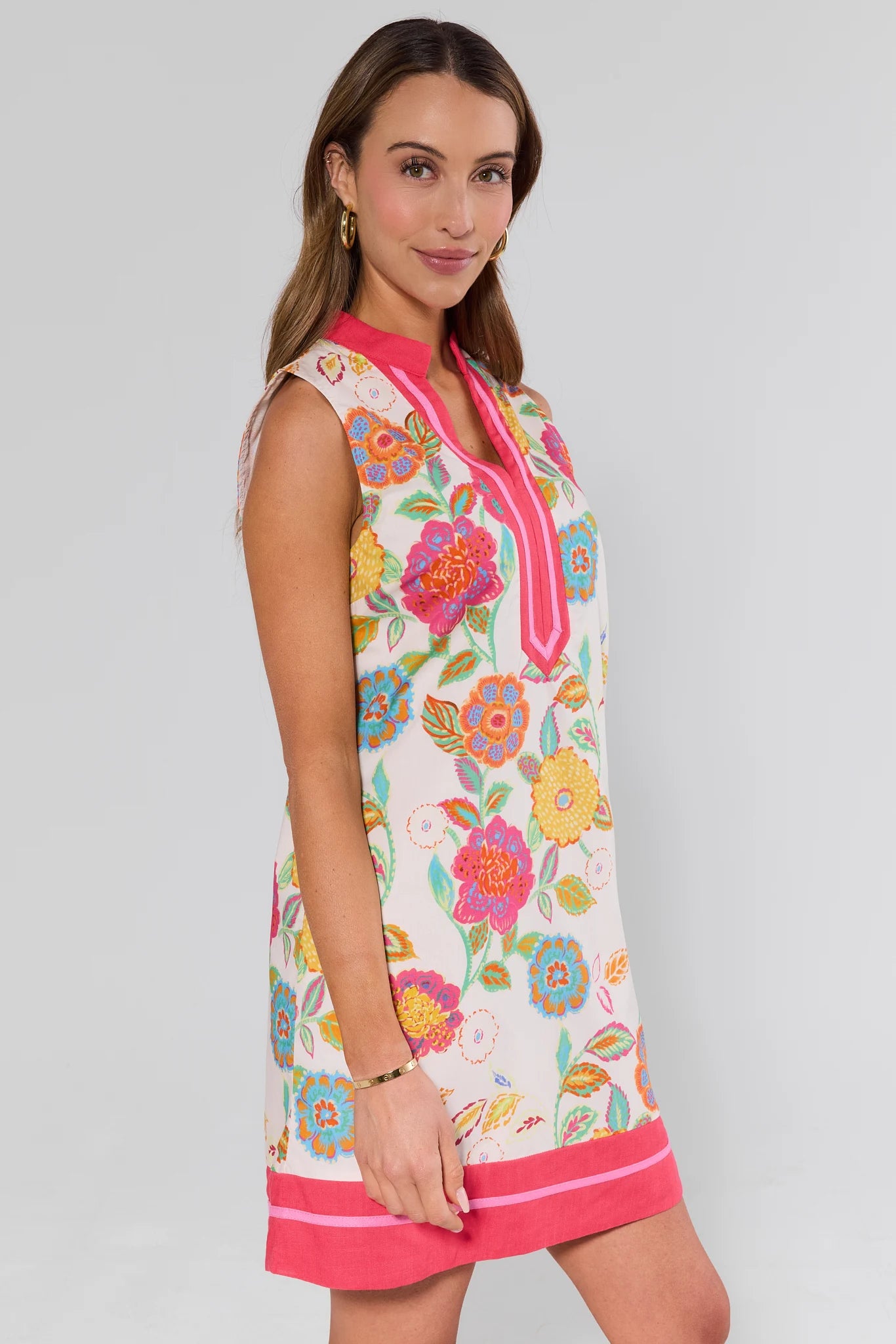 side shot Woman wearing a colorful floral dress with a pink trim on a plain background