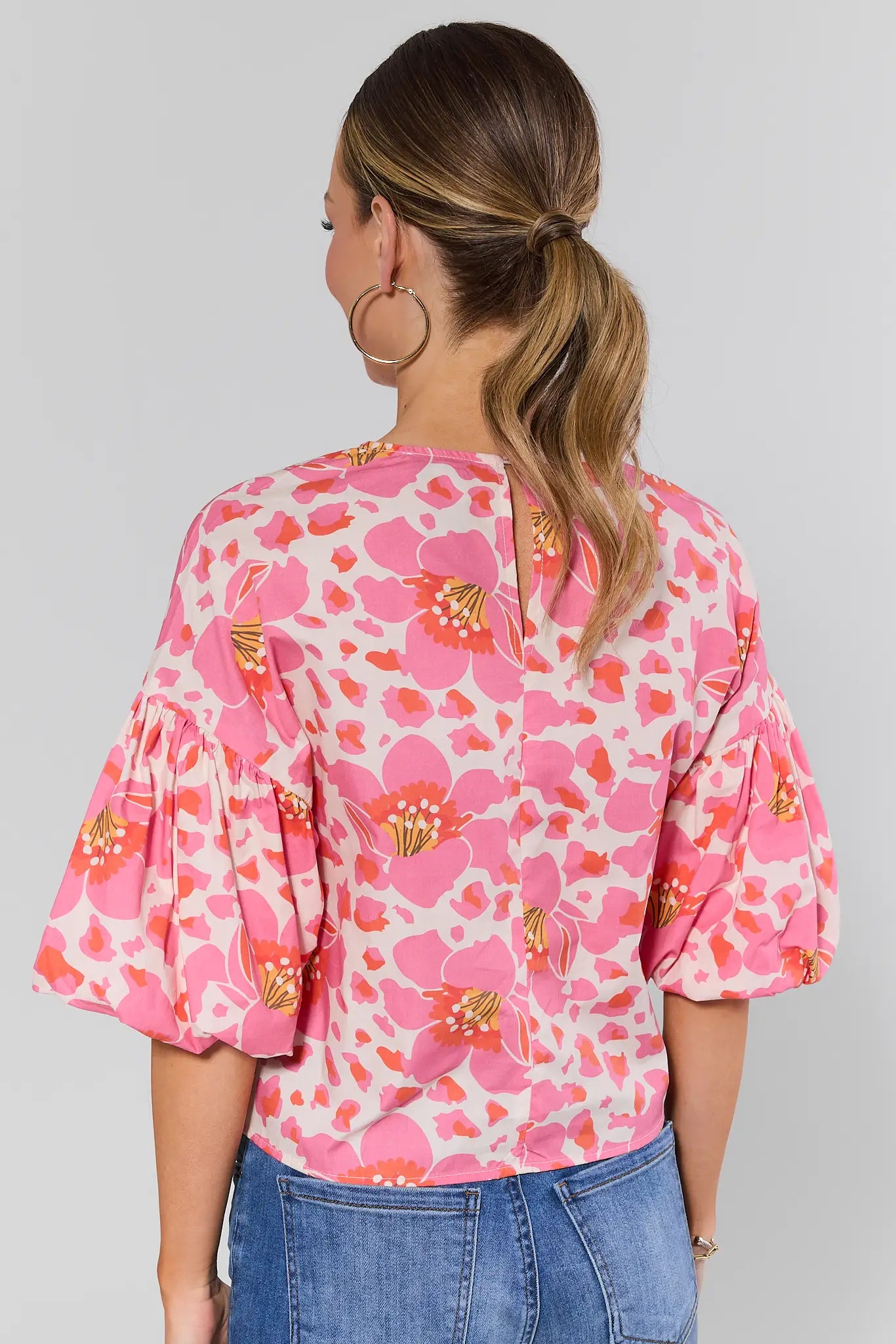 Woman standing wearing a pink floral blouse with blue jeans on a gray background