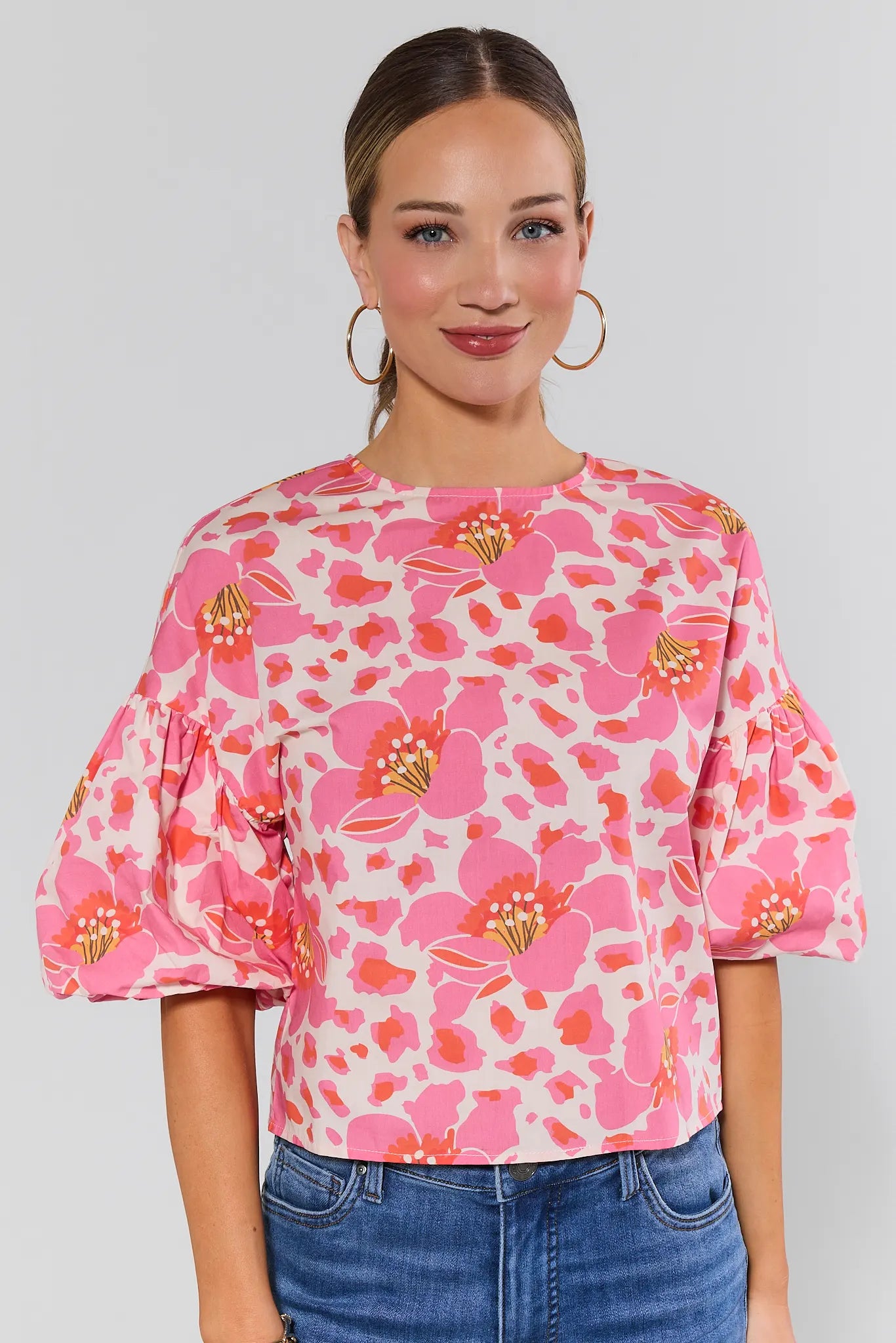 Woman wearing a pink floral blouse with blue jeans on a plain background
