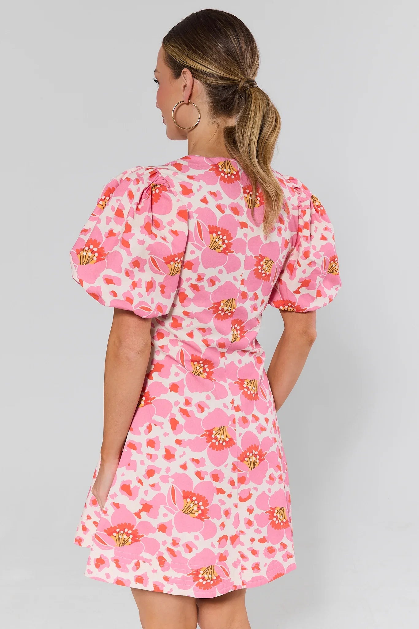 Woman standing wearing a pink floral dress against a plain background